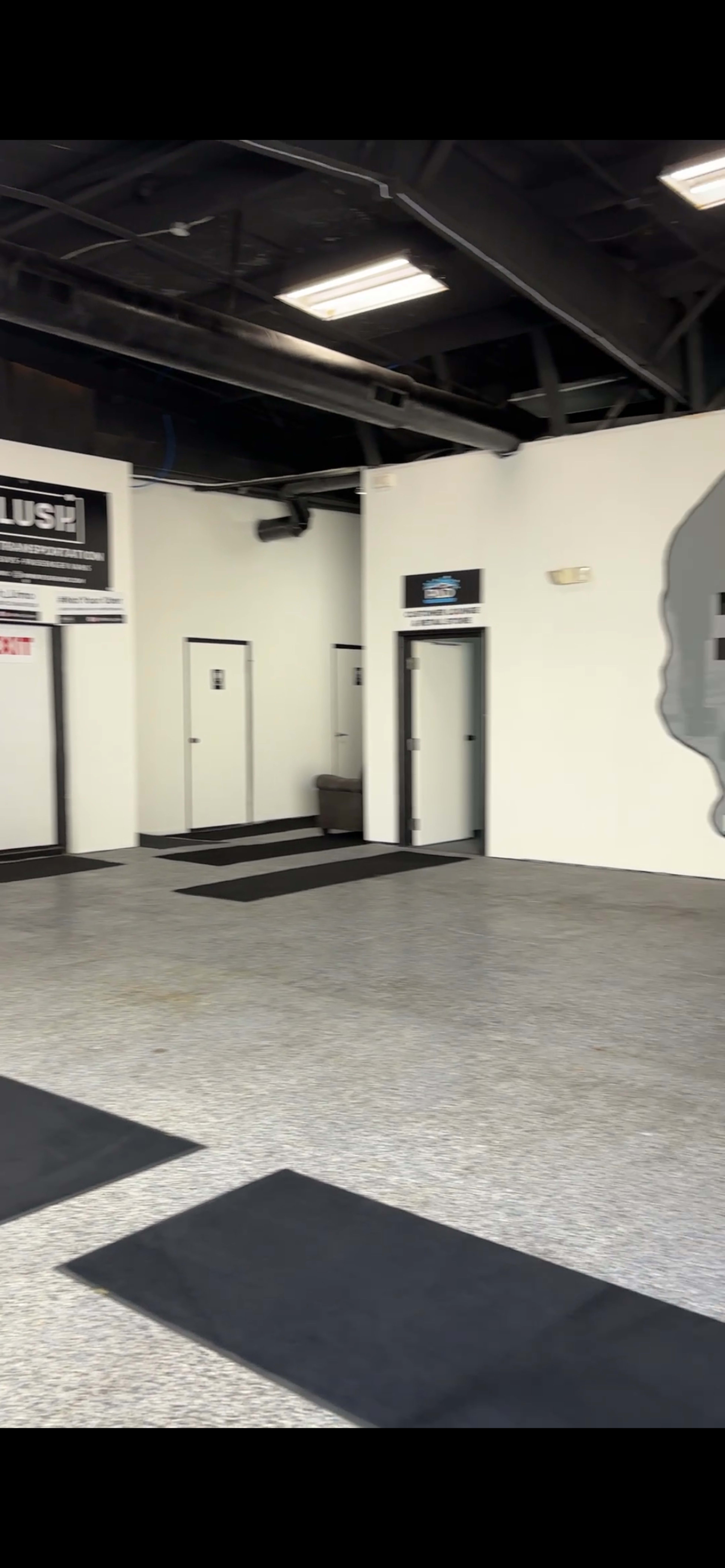 The image shows a spacious, empty room with a polished concrete floor and several doors along the walls, including a large mural on one side.