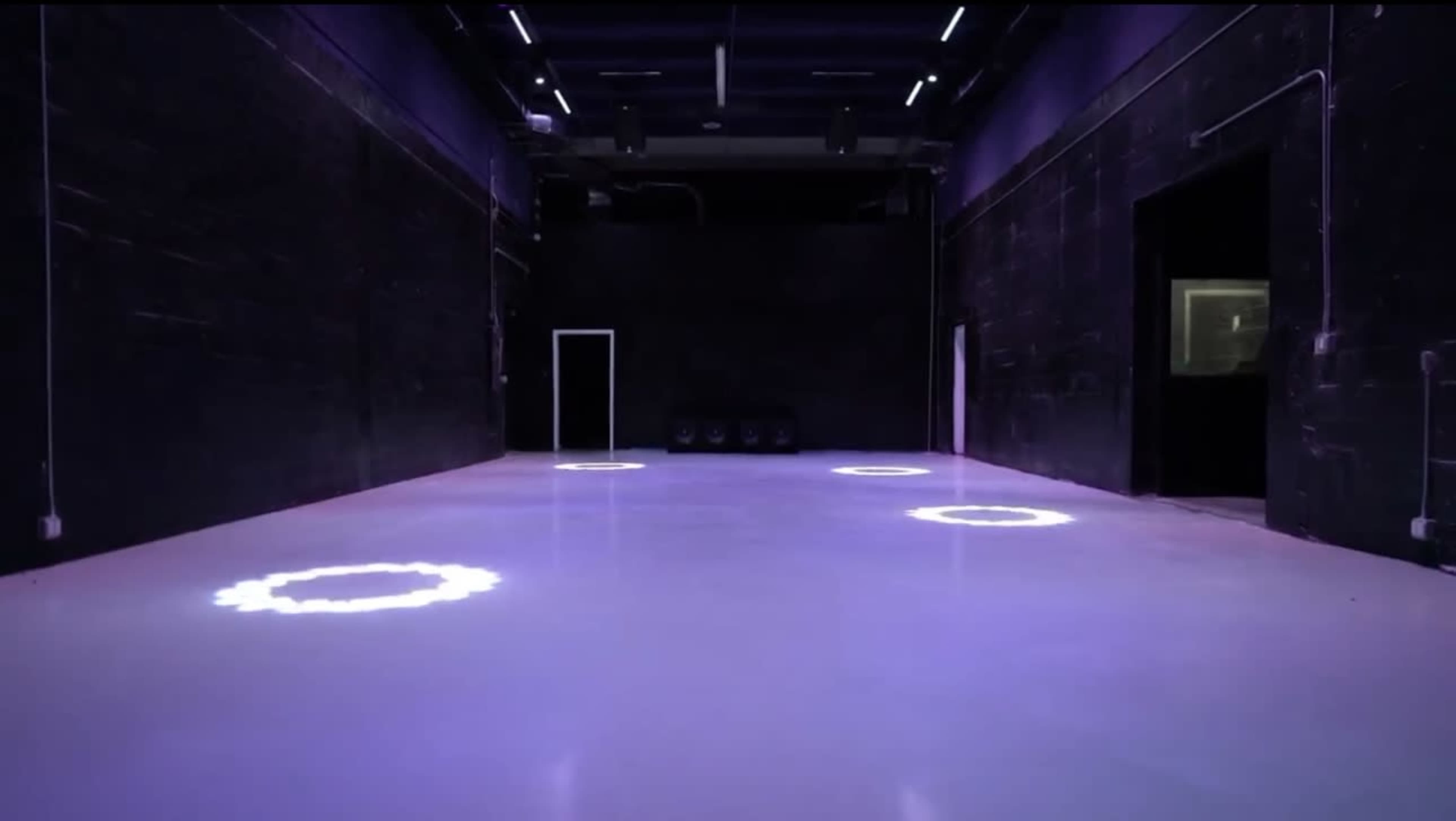 The image shows an empty, dimly lit room with circular light patterns on the polished floor.