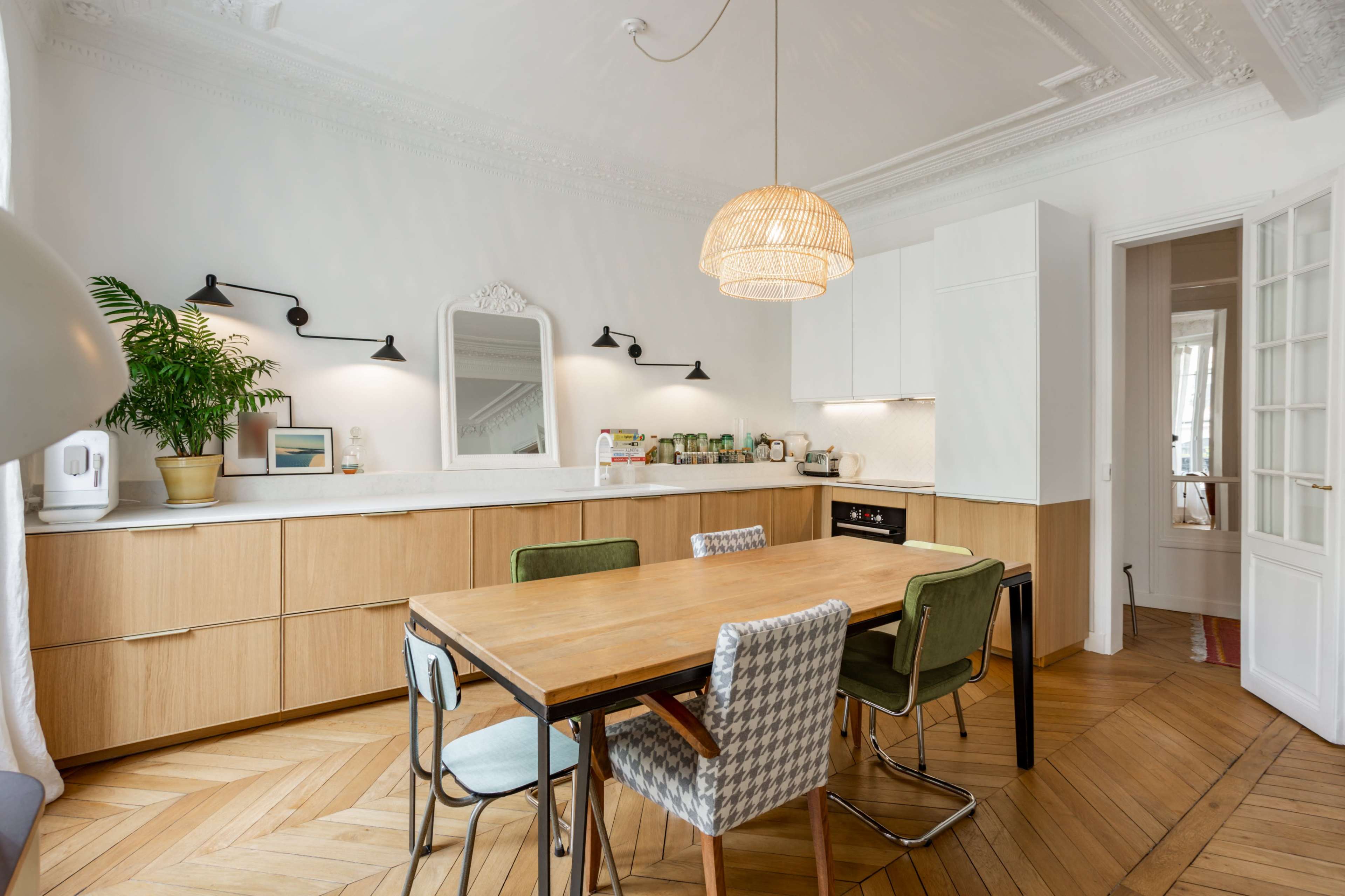 A modern kitchen features wooden cabinetry, a large dining table with chairs, and a woven pendant light.