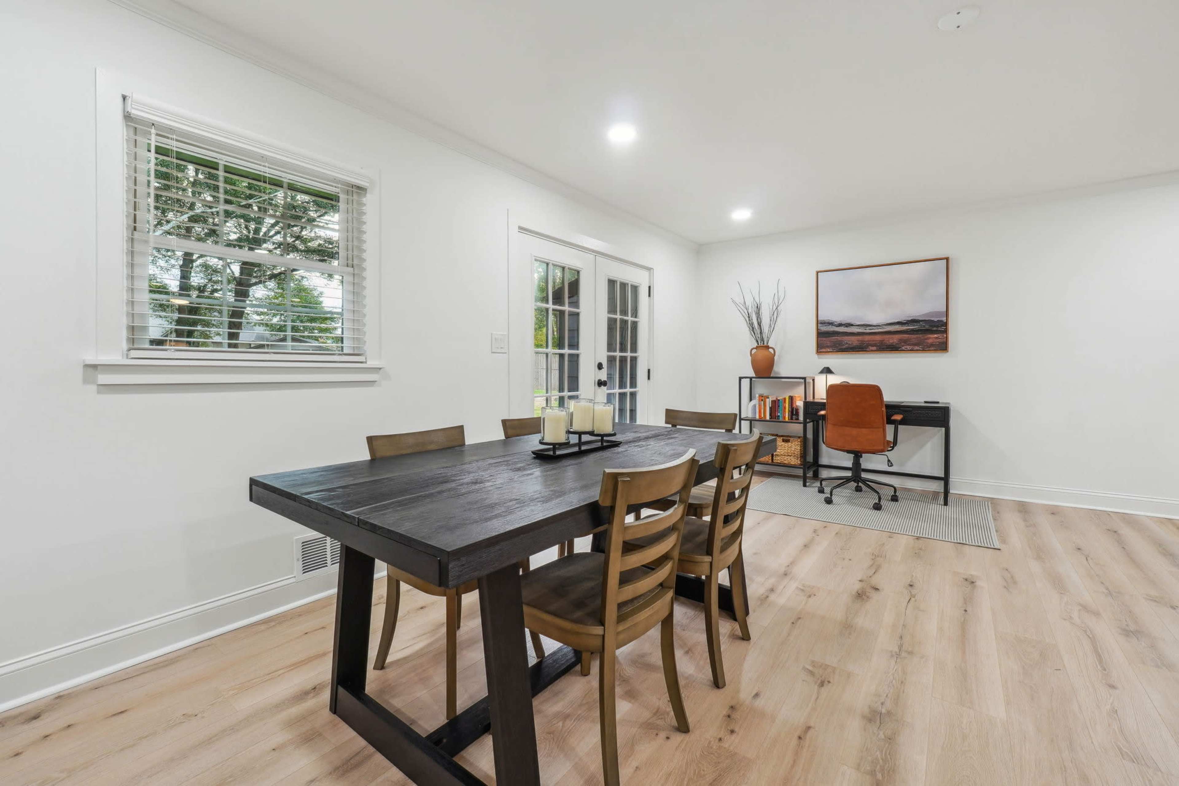 A dining area with a rectangular table and six chairs is adjacent to a home office setup against a light-colored wall.