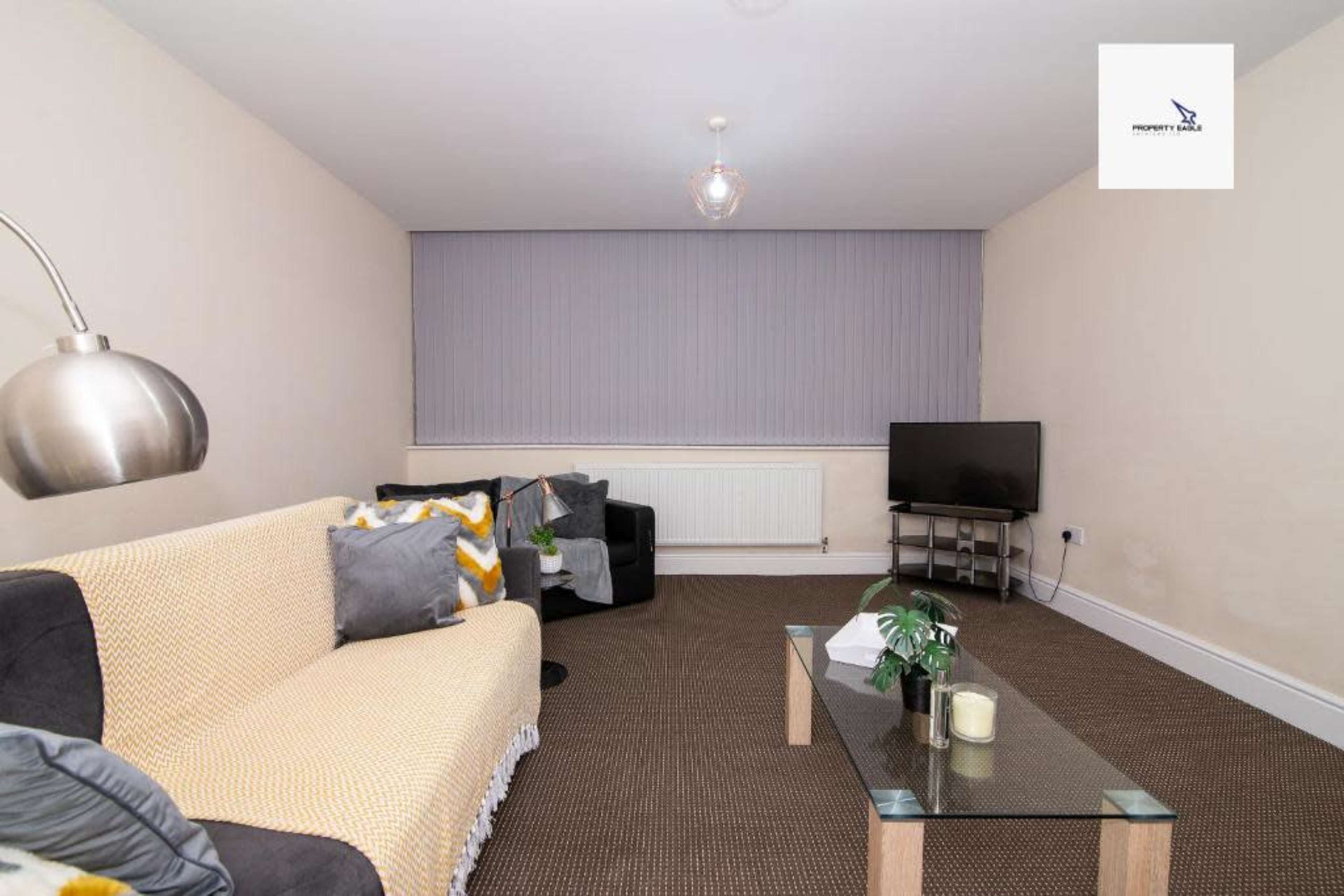 A living room featuring a sofa, an armchair, a coffee table, a television on a stand, and a window covered with blinds.