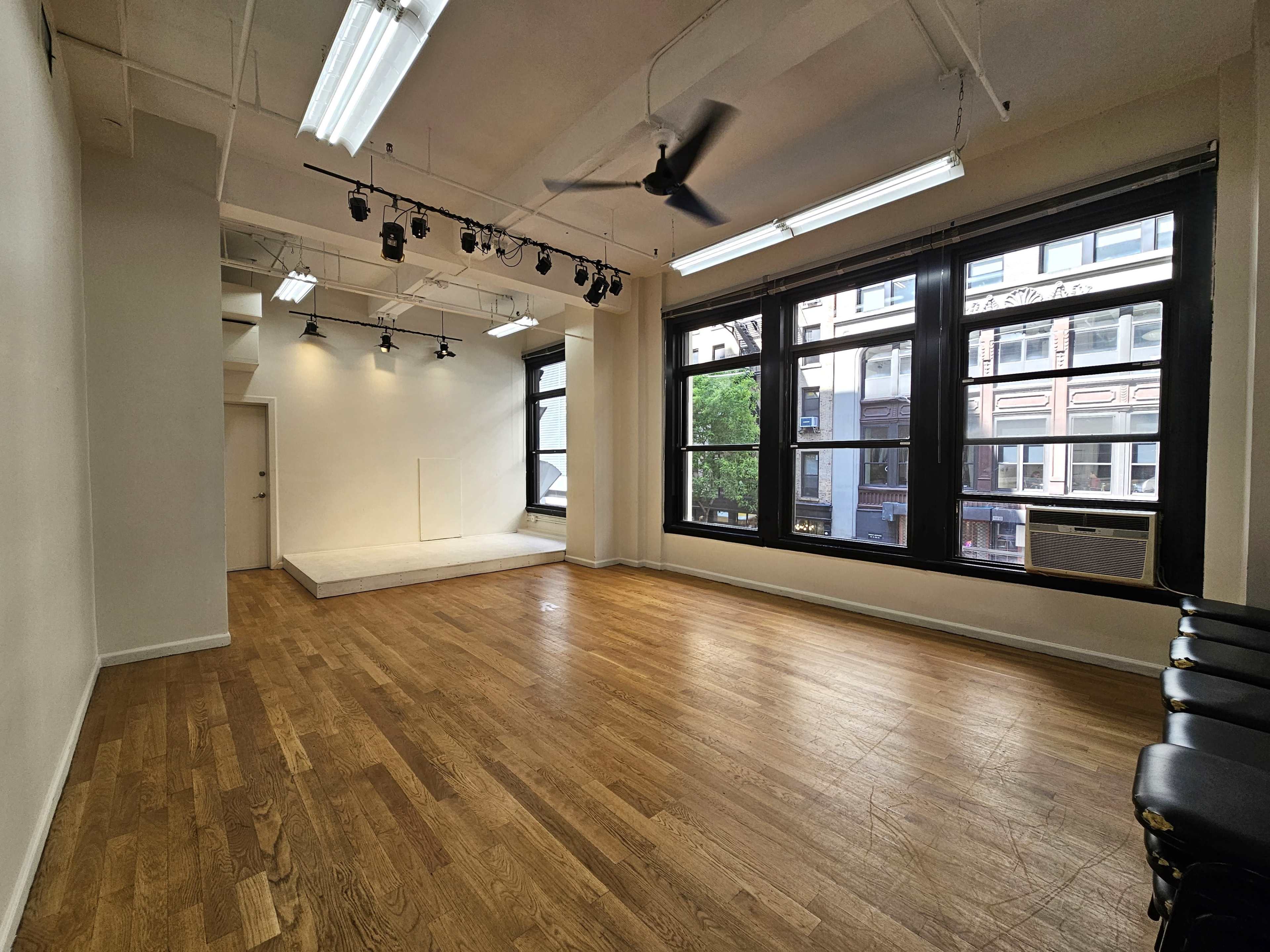 An empty room with wooden floors, large windows, and a raised platform in one corner.