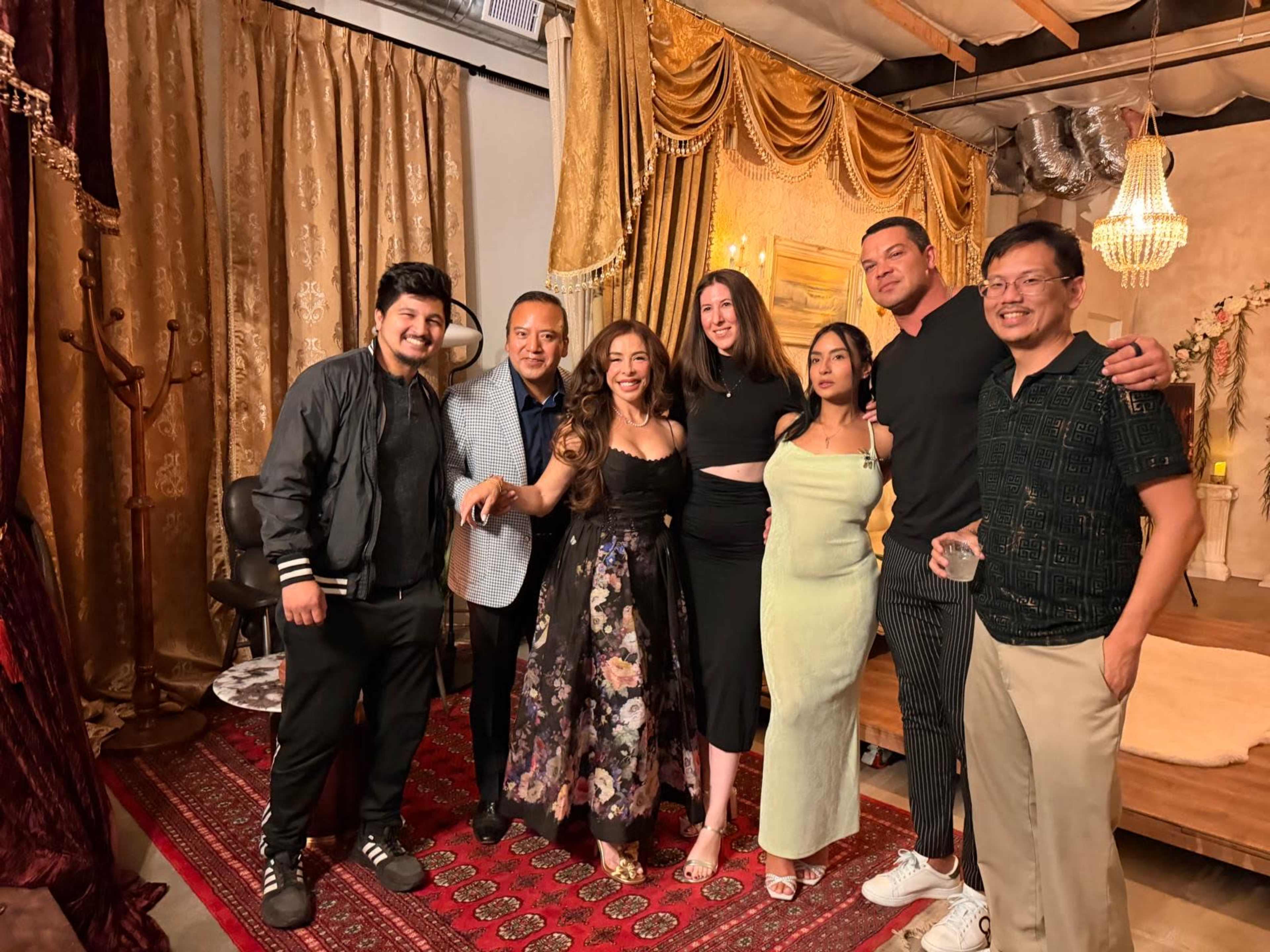 A group of six people poses for a photo in a decorated indoor space with curtains and a rug.