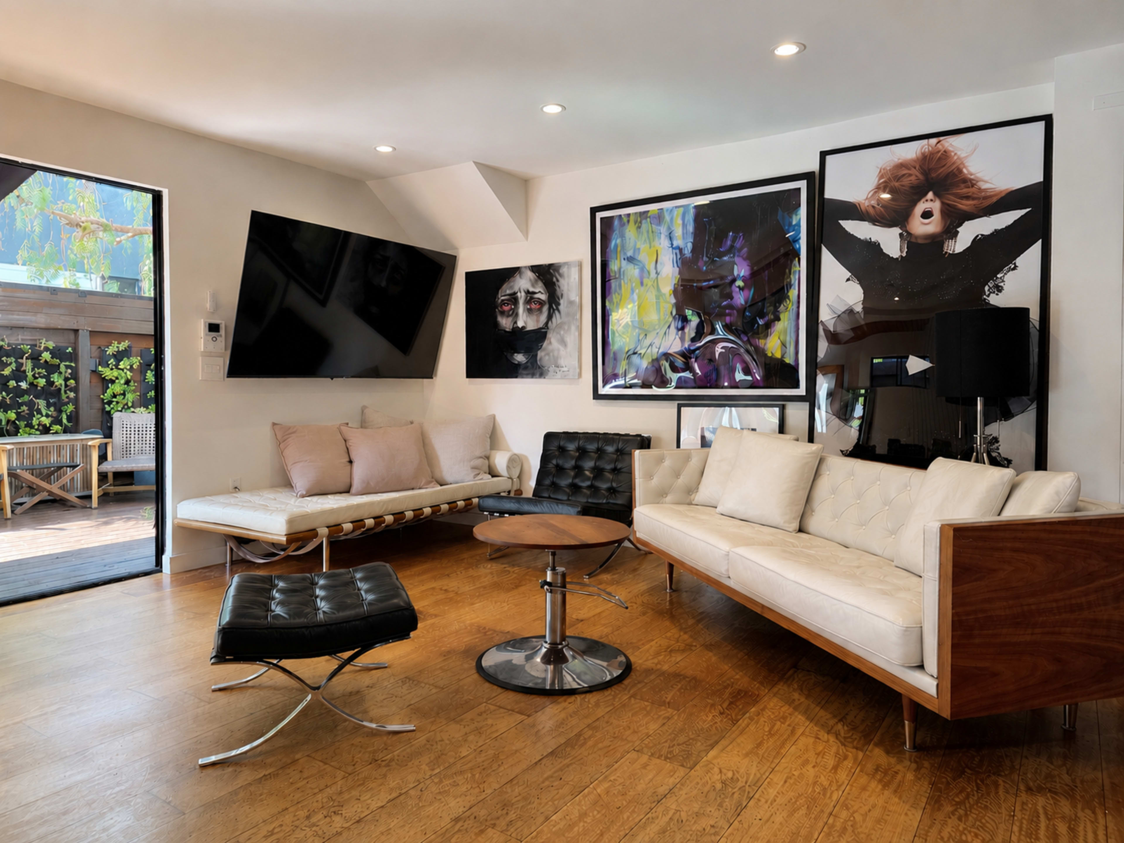 The living room features a modern design with a large flat-screen TV mounted on the wall, a sleek white sectional sofa, and two pieces of striking artwork displayed on the walls.