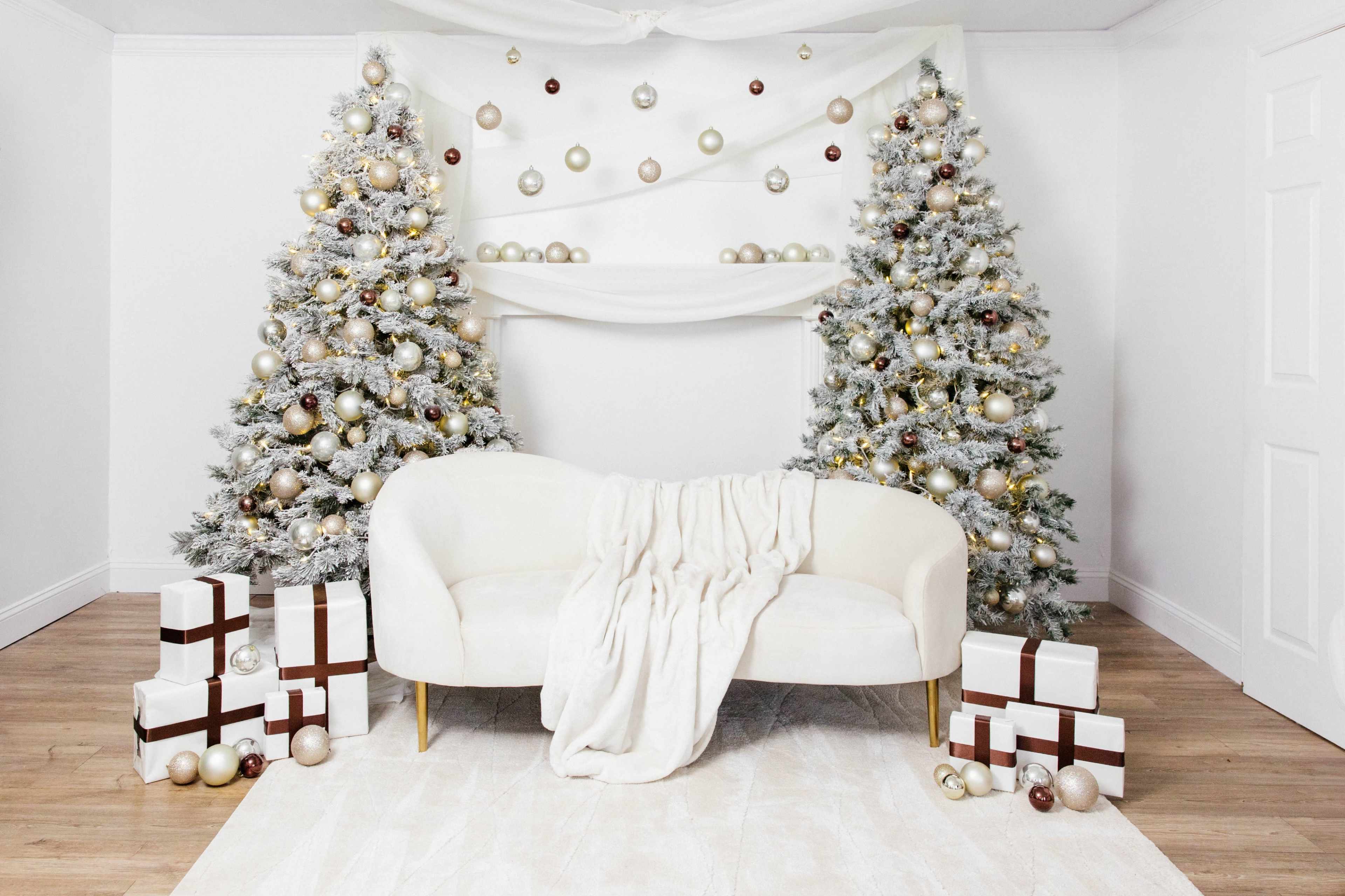 The image shows a decorated room with two Christmas trees and a white couch draped with a blanket, surrounded by wrapped presents.