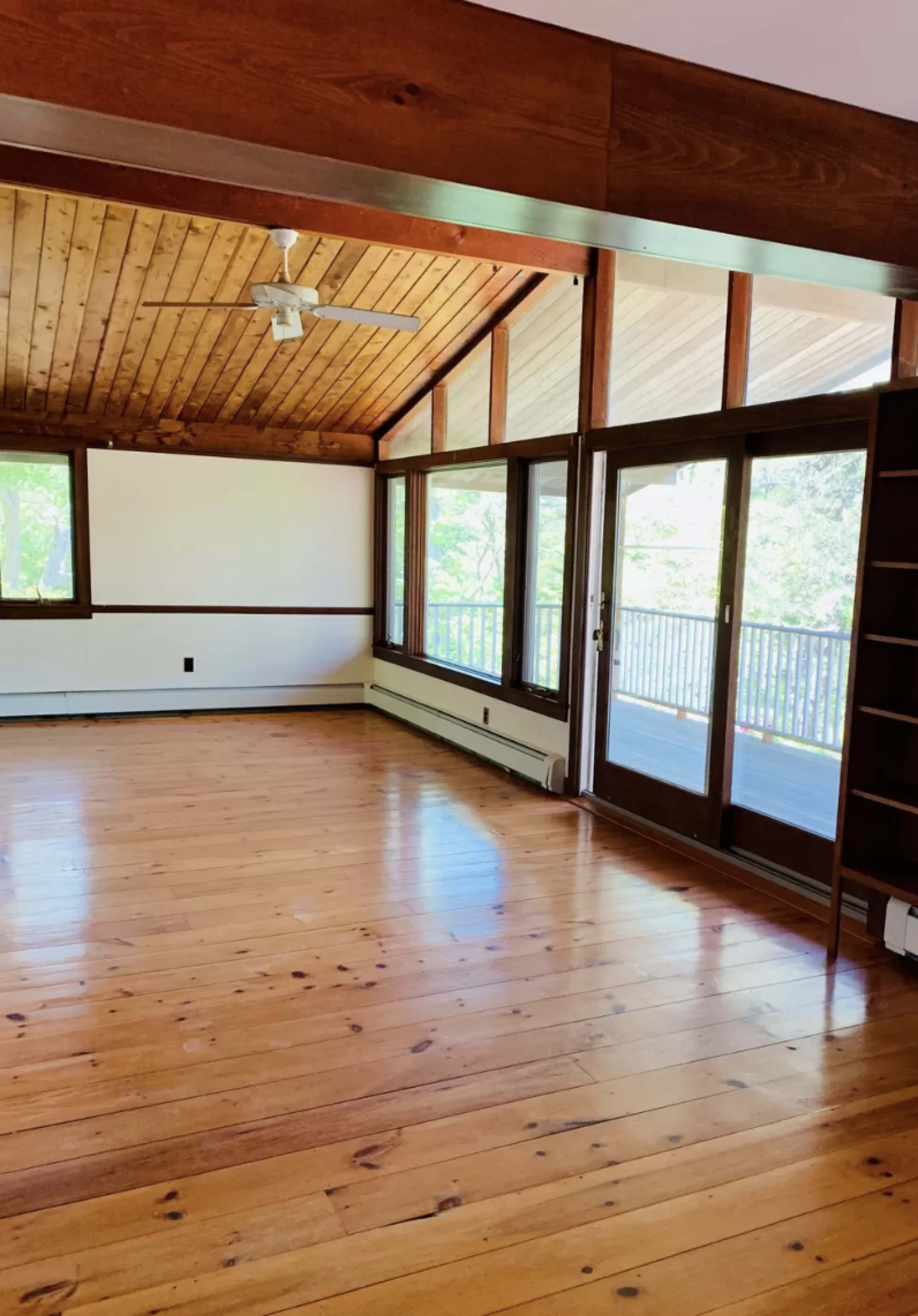 A spacious living room features wooden floors and a vaulted ceiling with large windows and sliding doors leading to a balcony.