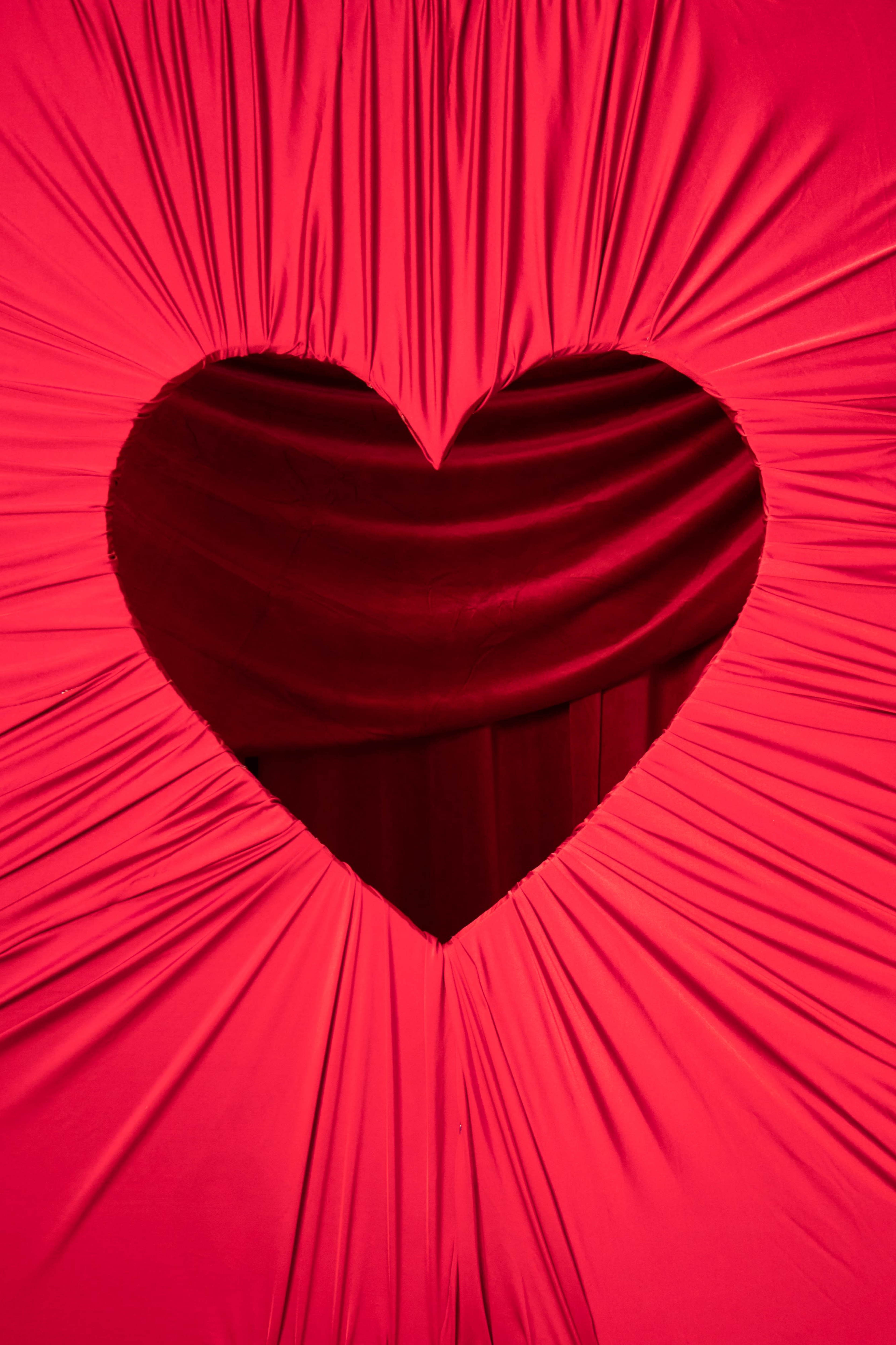 A large red fabric drape features a heart-shaped cutout revealing a darker red background.