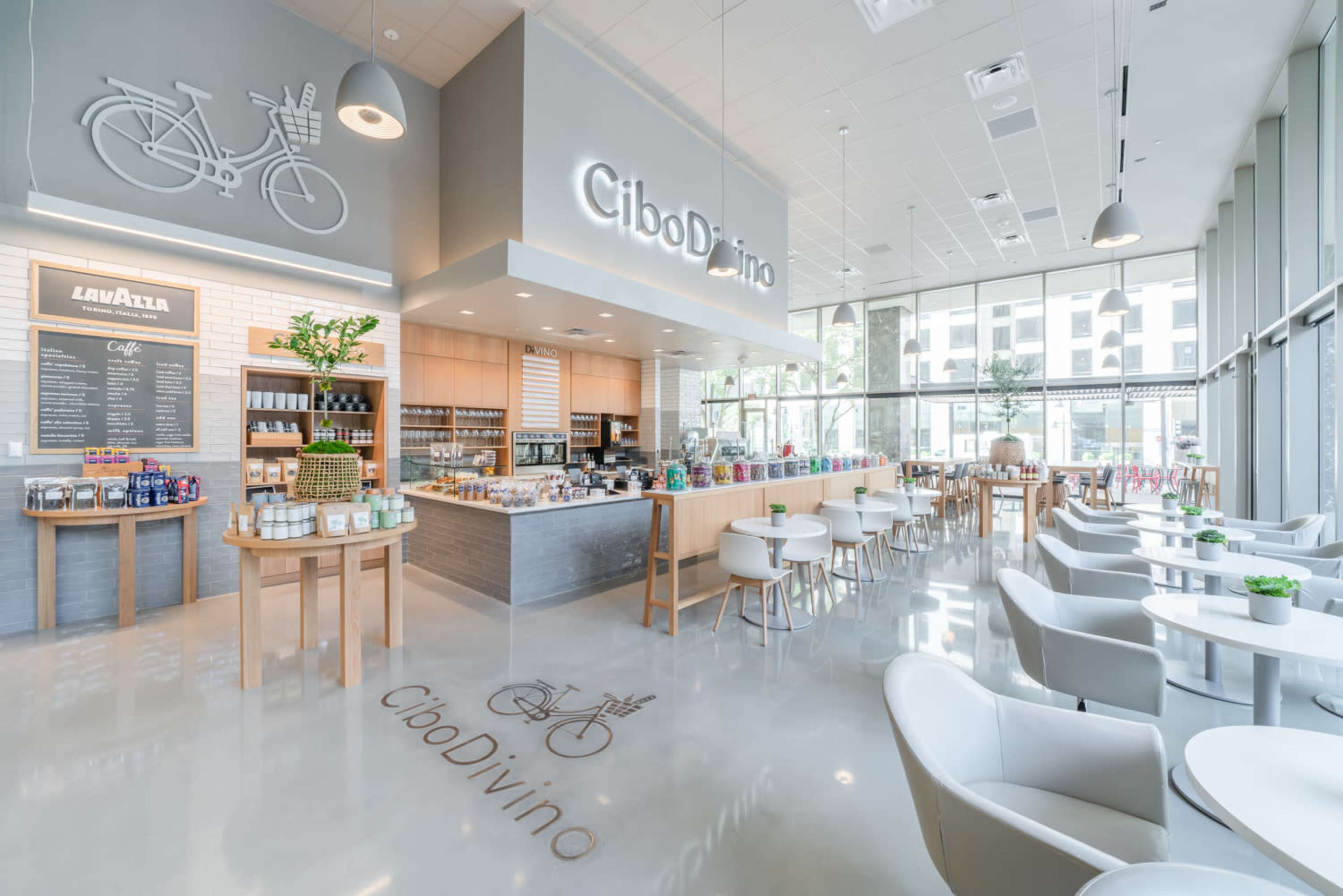 The image shows a modern café interior with a display counter, seating areas, and large windows allowing natural light.
