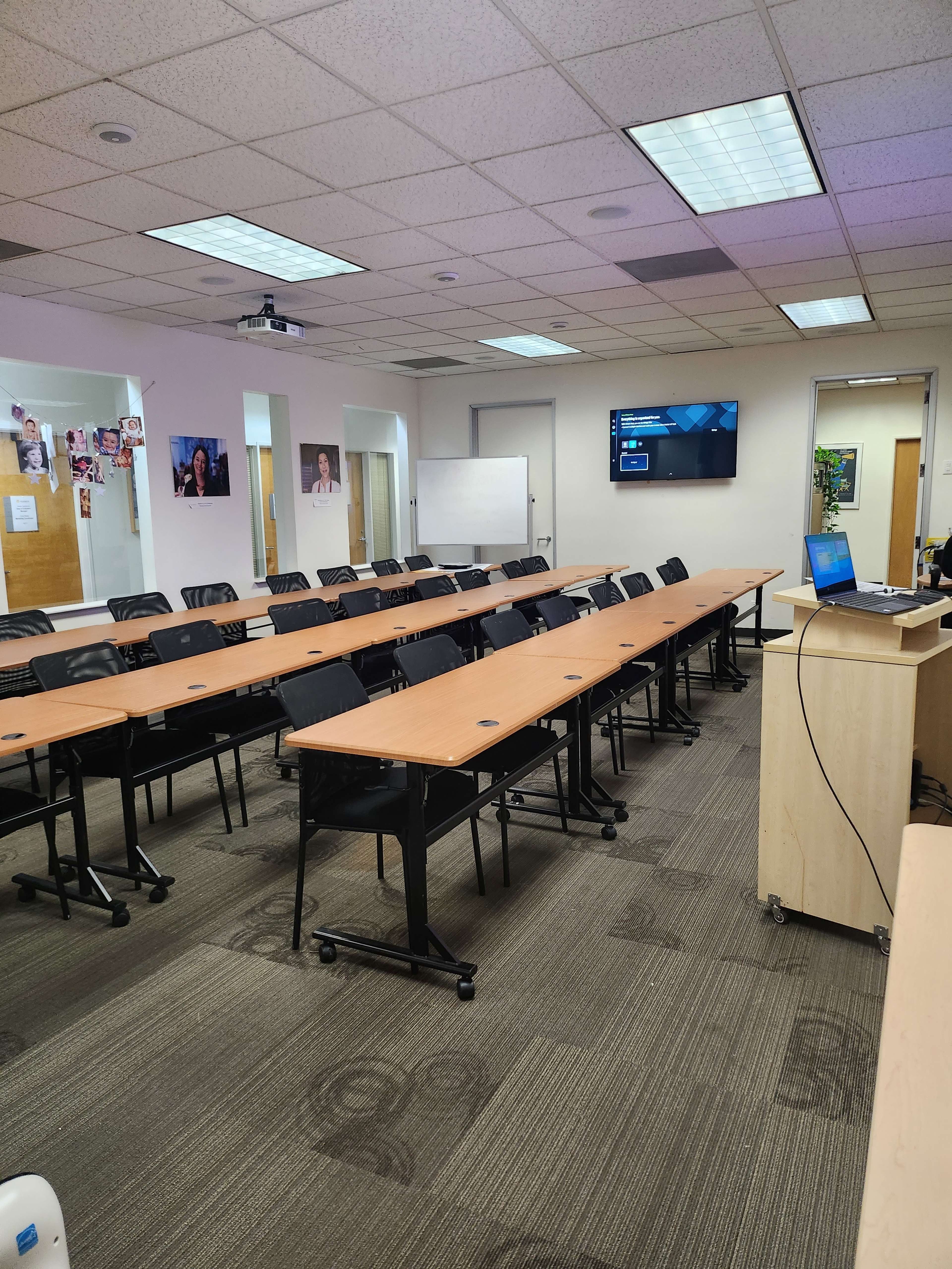 A modern conference room features rows of tables and chairs, a projector, and a large screen on the wall.