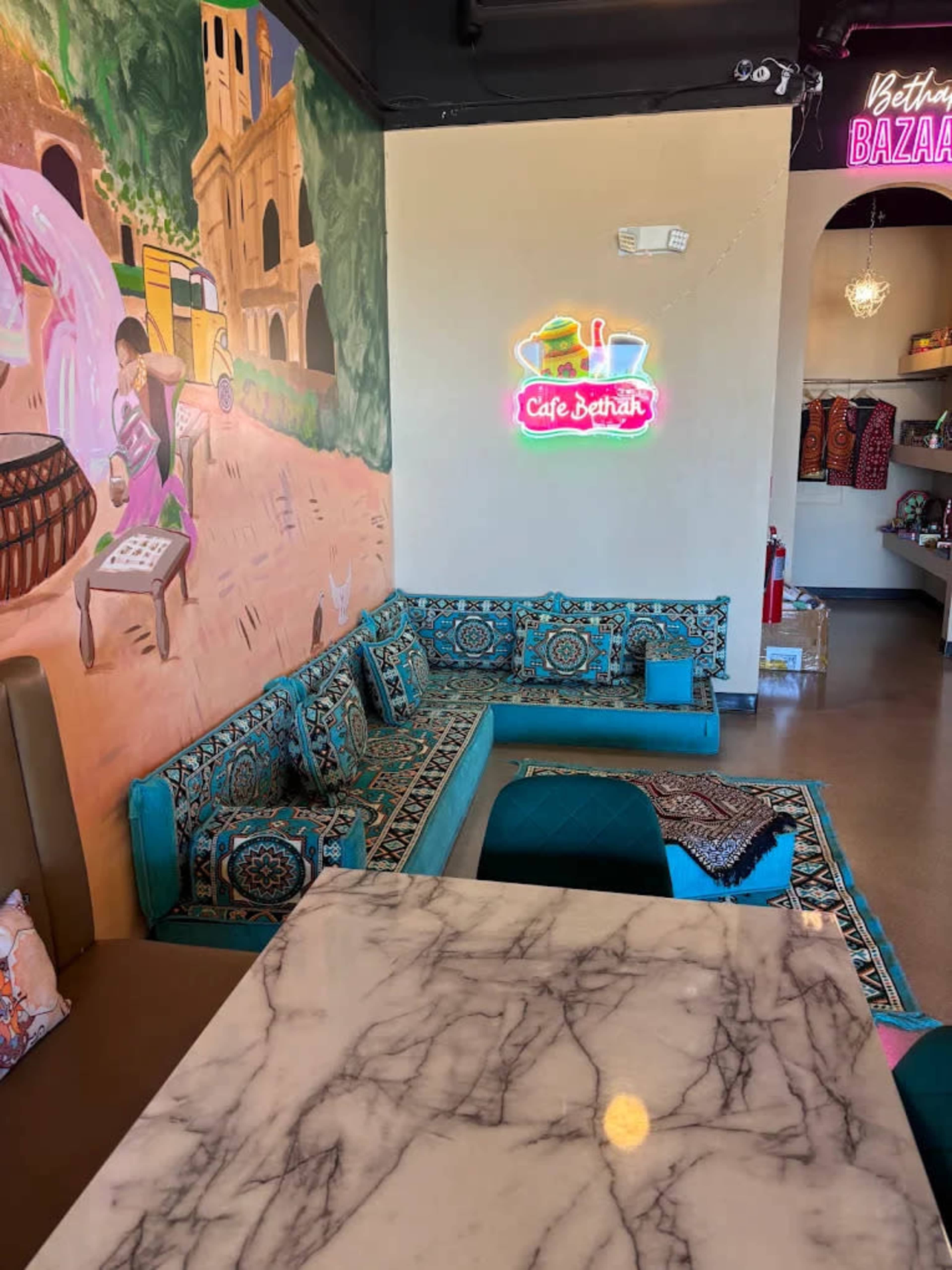 The image shows a cozy café interior with vibrant wall art, a patterned seating area, and a marble table.
