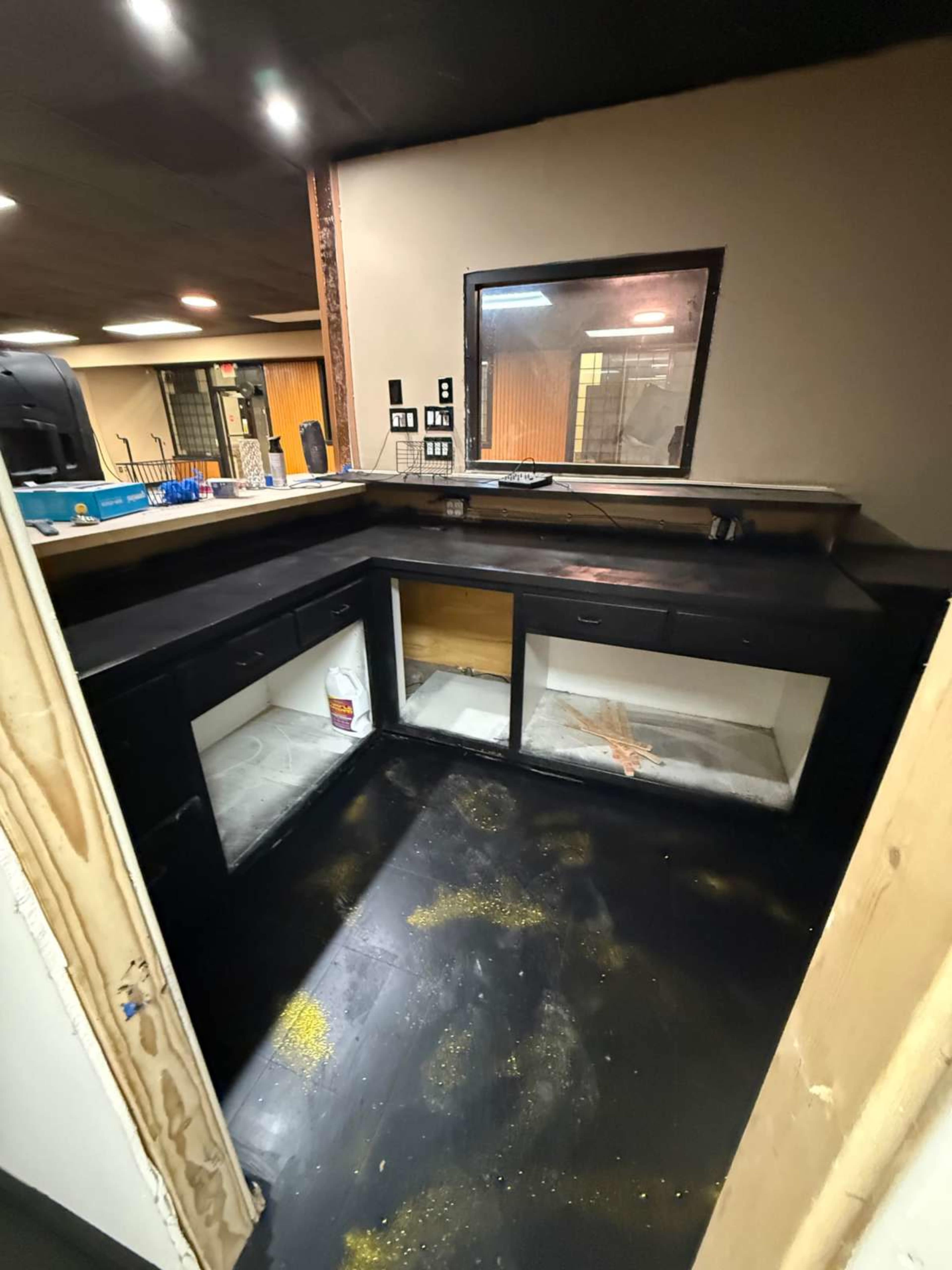 The image shows a partially unfinished kitchen area with black cabinets and floor, featuring a large window and tools on the countertop.