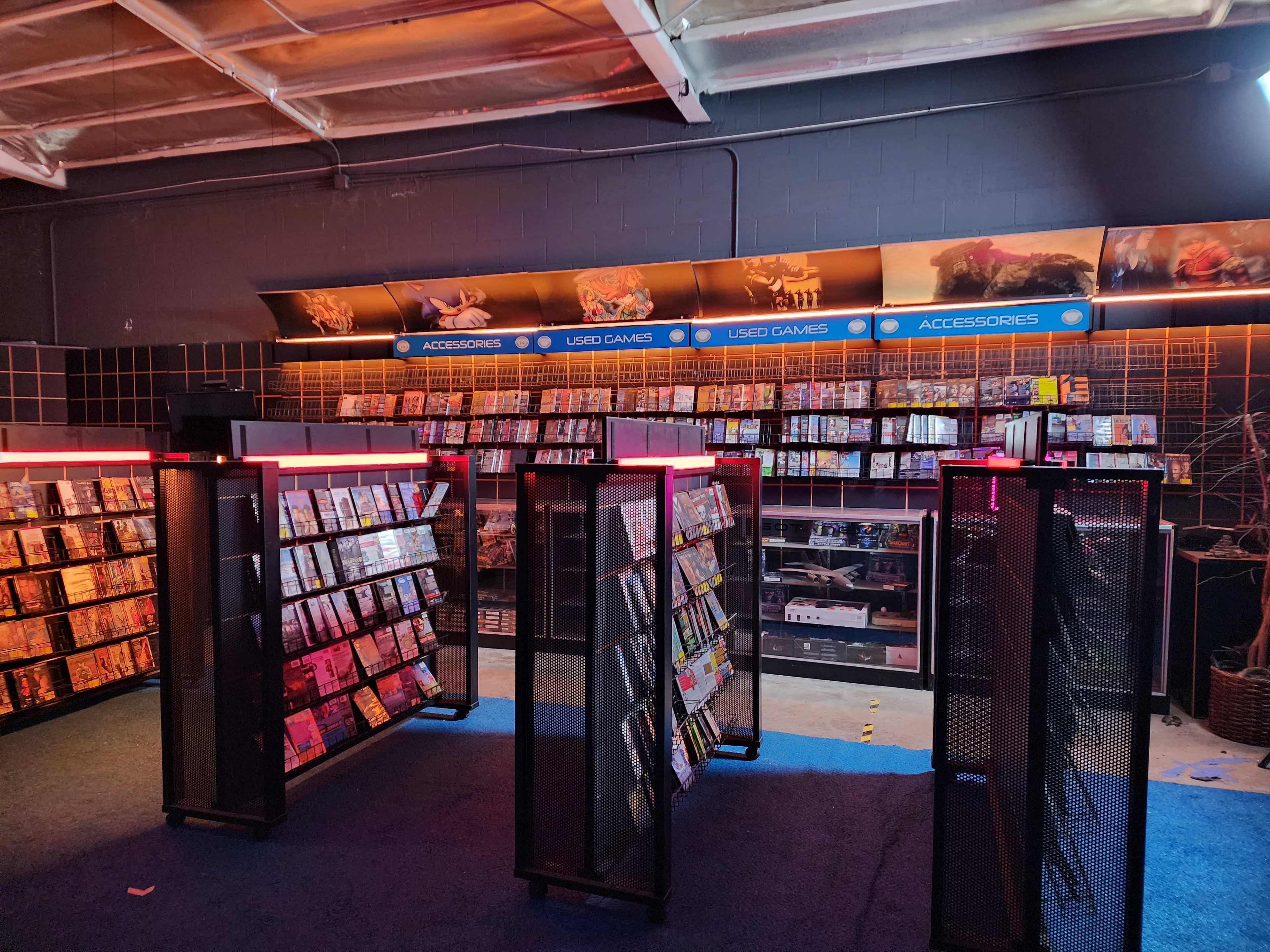 The image shows an interior of a retail space with shelves filled with DVDs and video games, illuminated by red lighting.