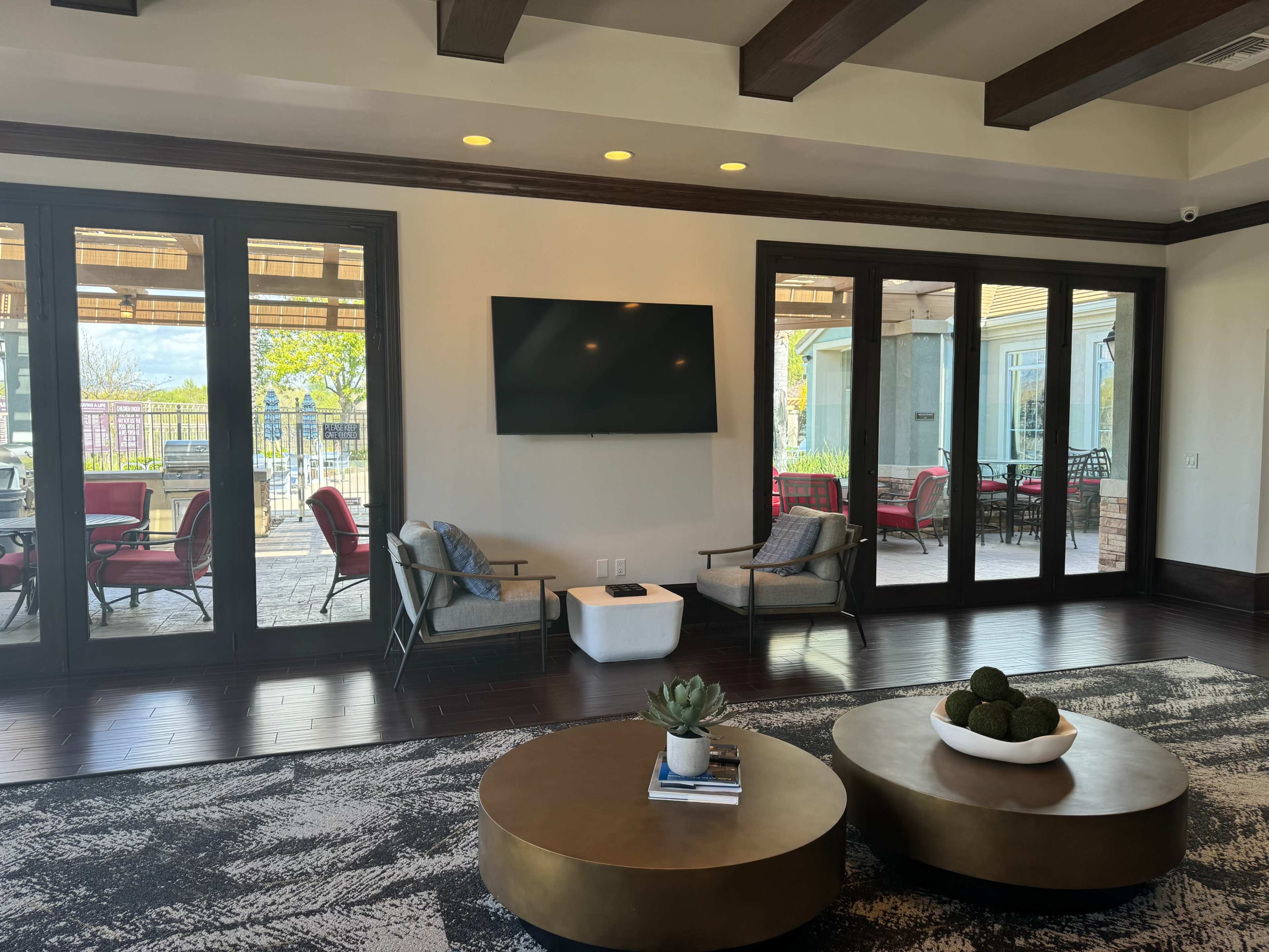 A modern living room with a television mounted on the wall, two chairs, a coffee table, and large glass doors leading to an outdoor patio.
