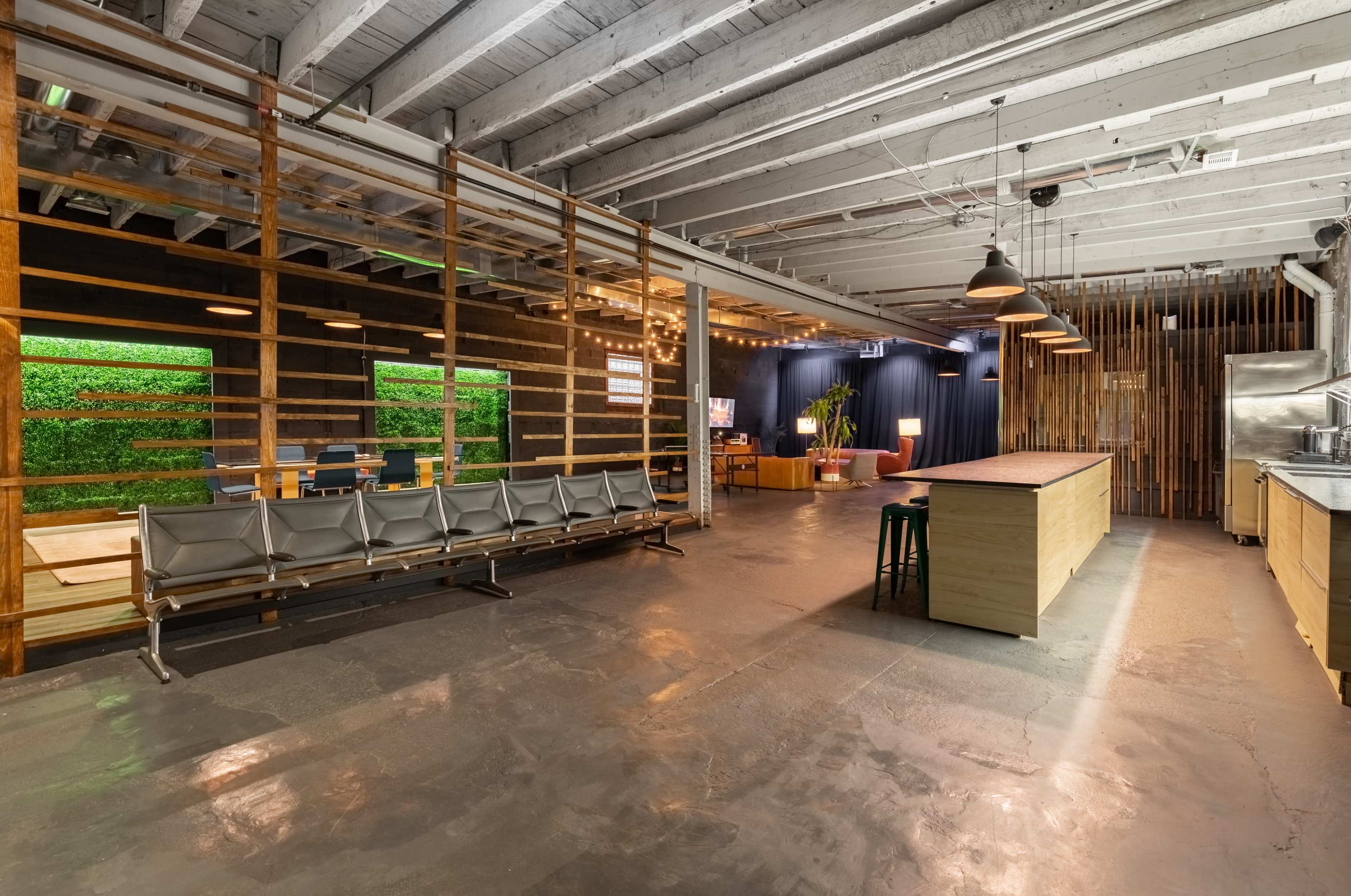 The image shows a spacious, modern interior with a waiting area featuring metal benches, a large counter, and greenery integrated into the design.