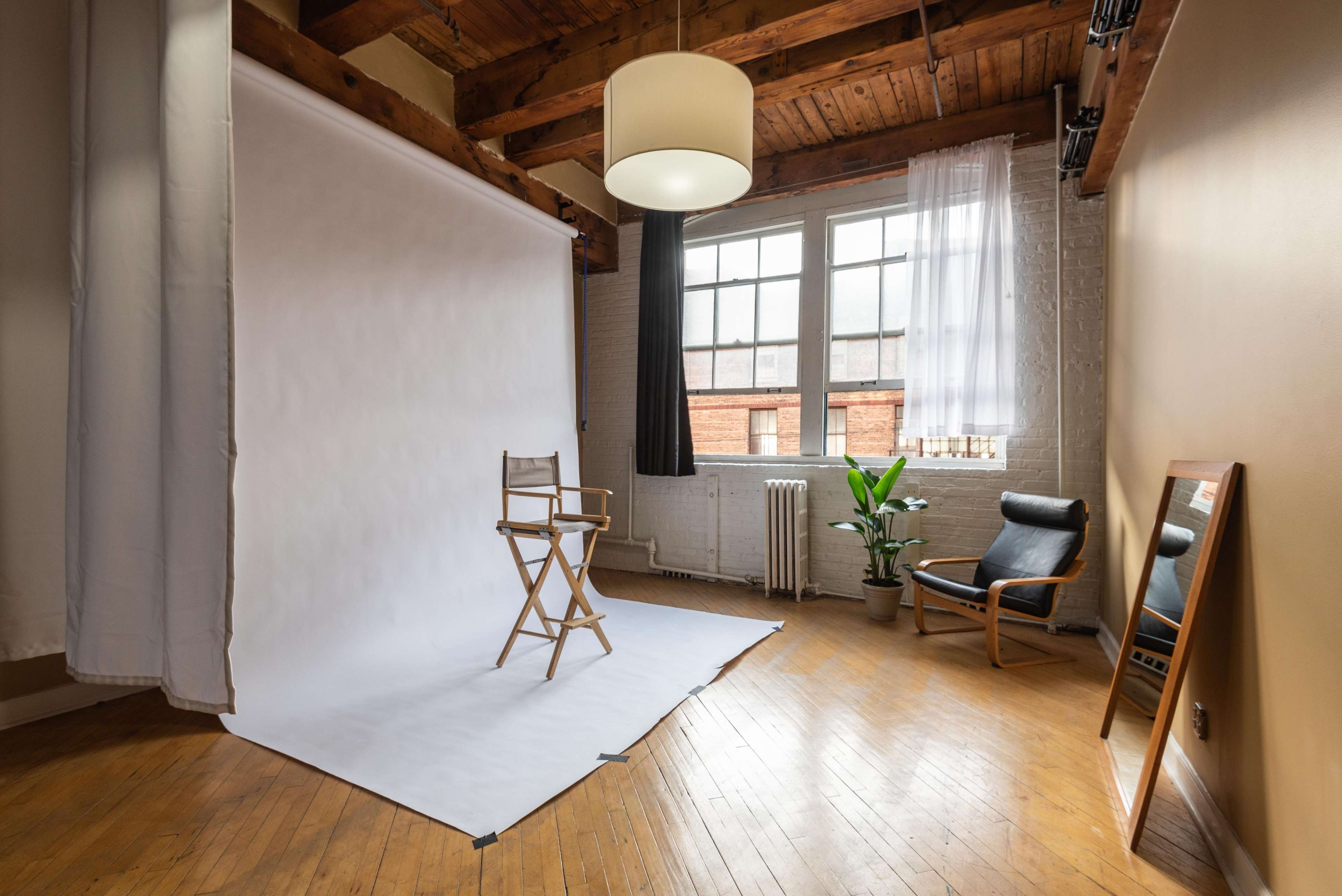 A minimalist photo studio with a white backdrop, a director's chair in the center, and a cozy seating area featuring a plant and a mirror.