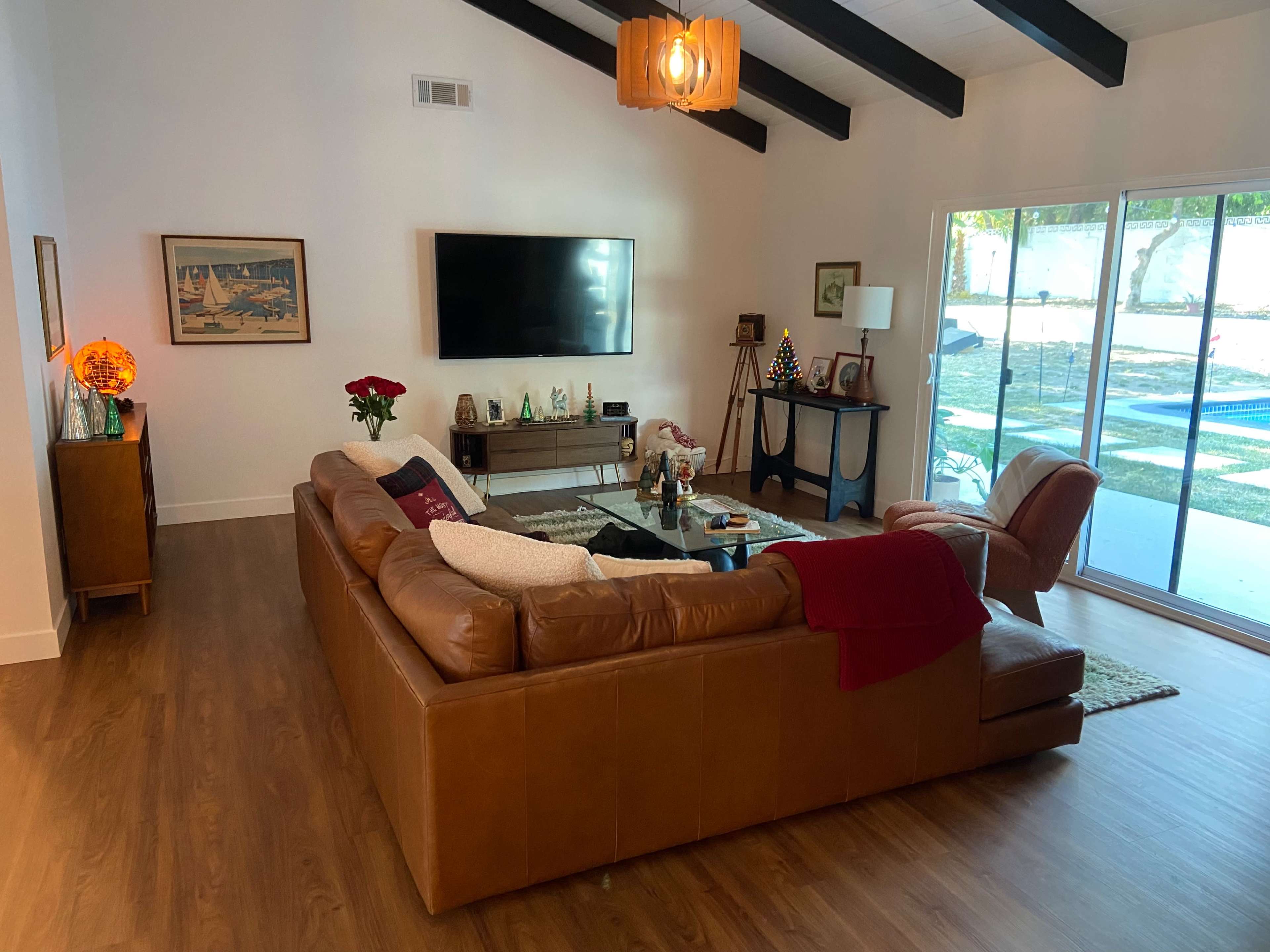 A spacious living room features a brown leather sectional sofa, a coffee table, and large windows overlooking a yard.