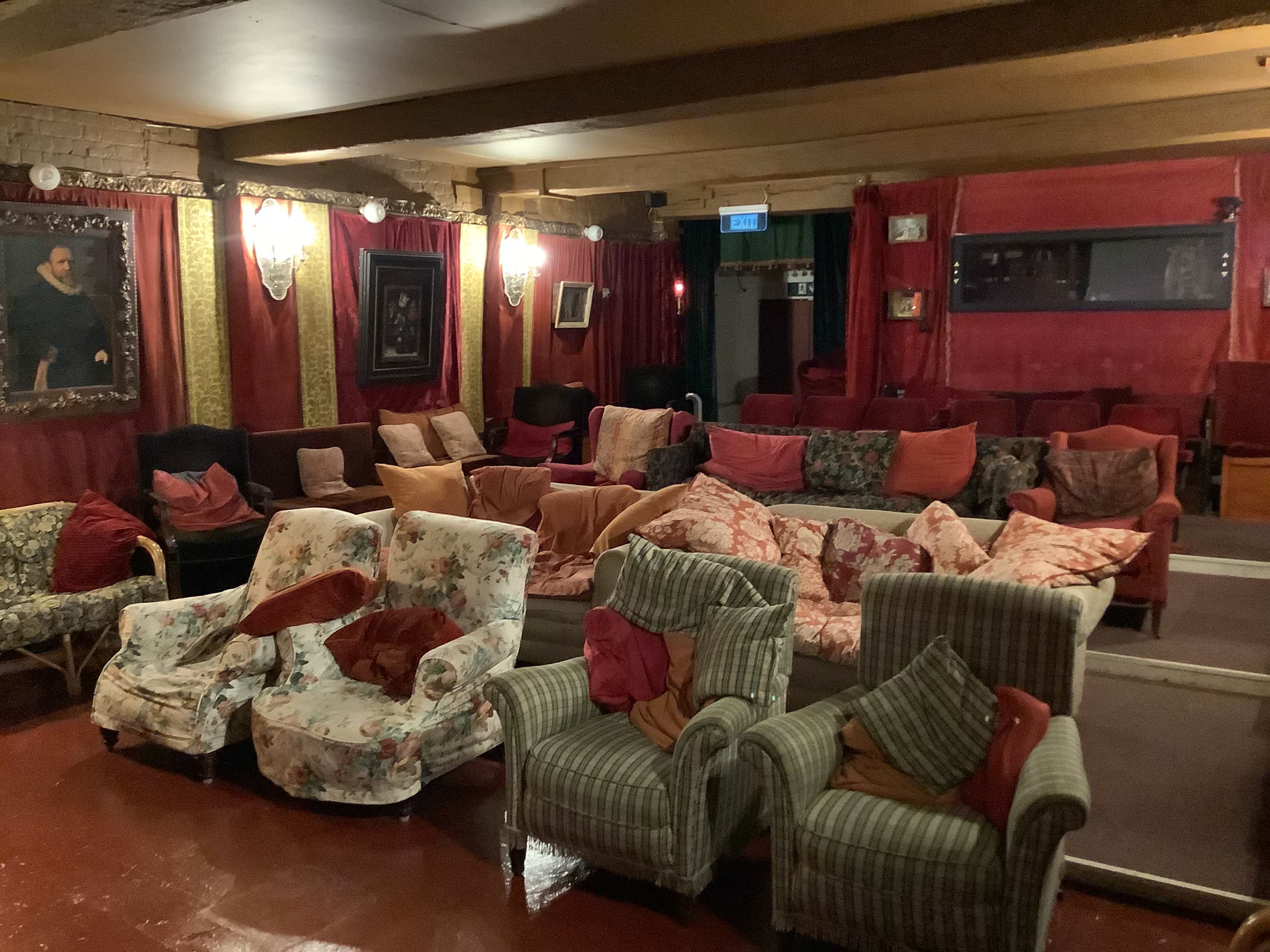 A room with a variety of mismatched sofas and armchairs arranged in a seating area, with red drapes and wall art in the background.