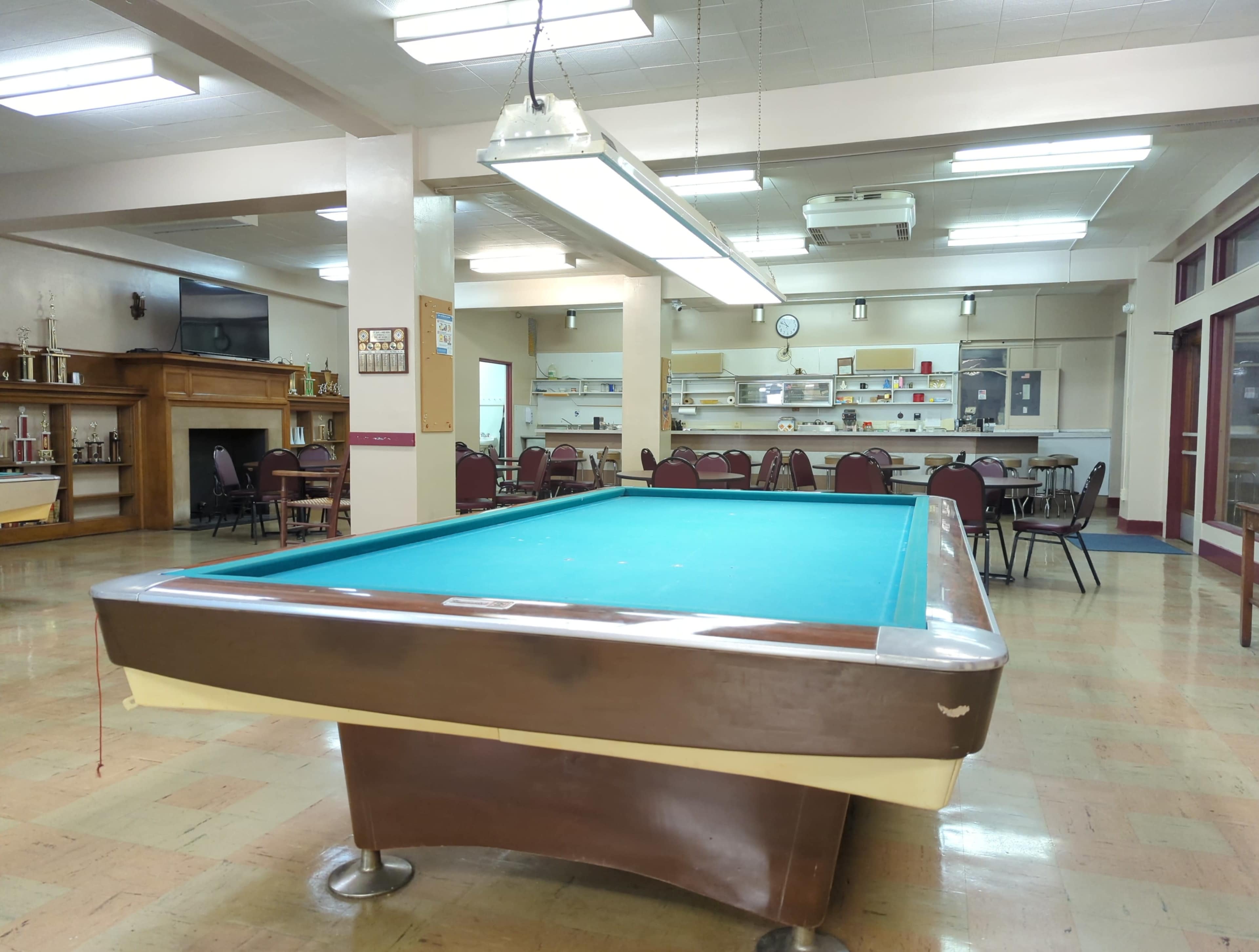 A billiards table in a spacious room with tables and chairs in the background.