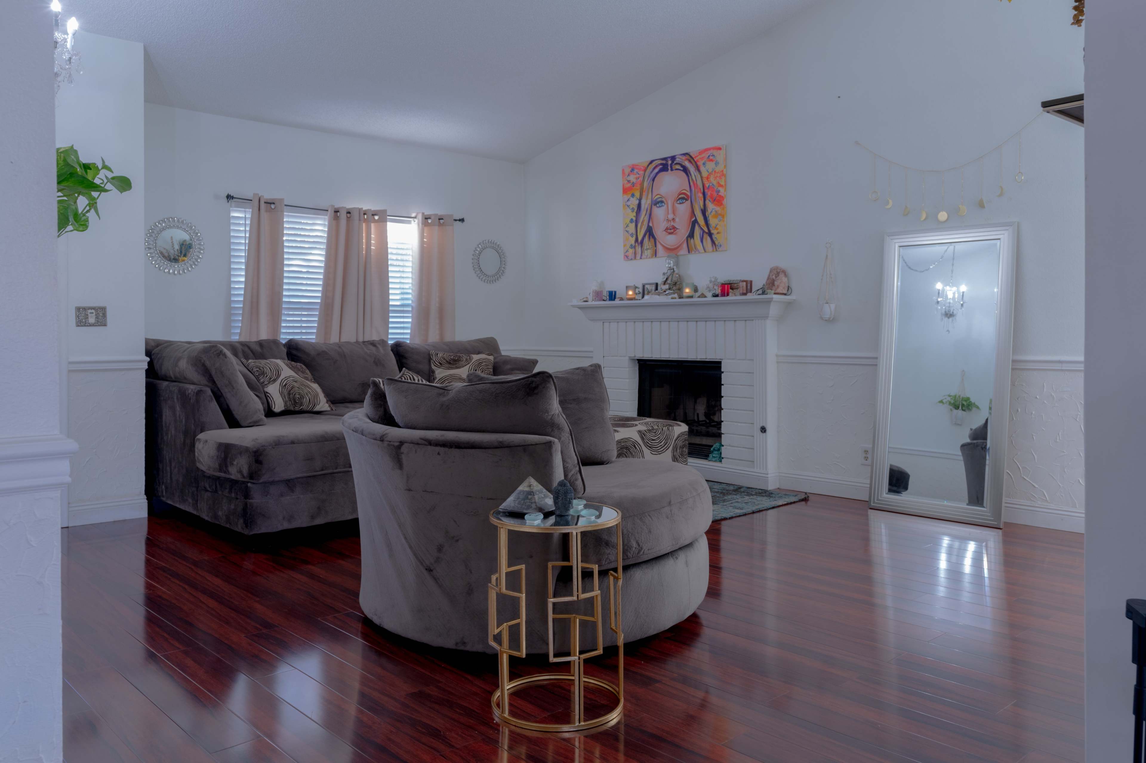 A spacious living room features a large sectional sofa, a circular side table, a fireplace, and a full-length mirror against the wall.