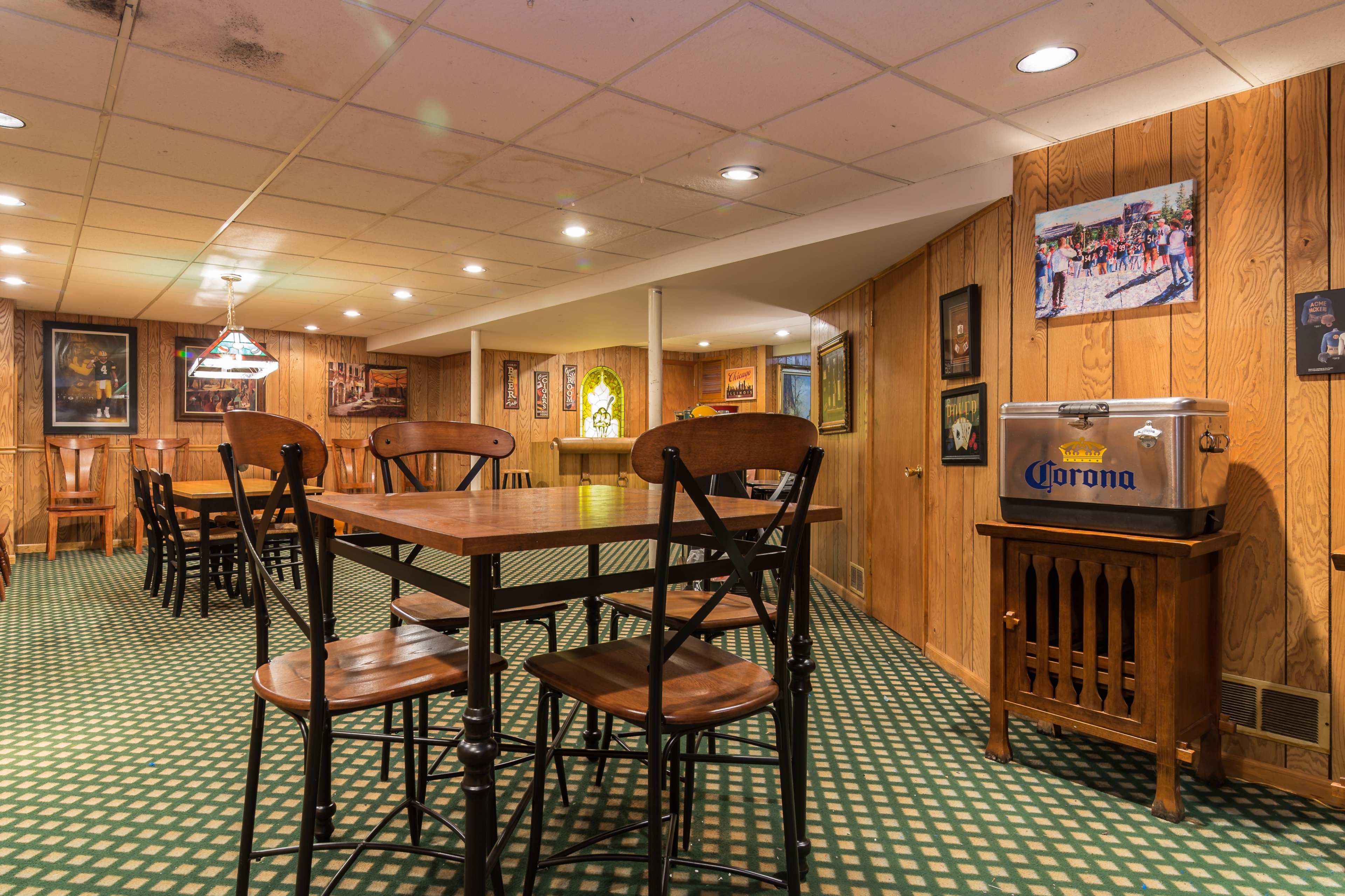 A dimly lit basement recreation area with wooden paneling, several tables and chairs, and framed photographs on the walls.