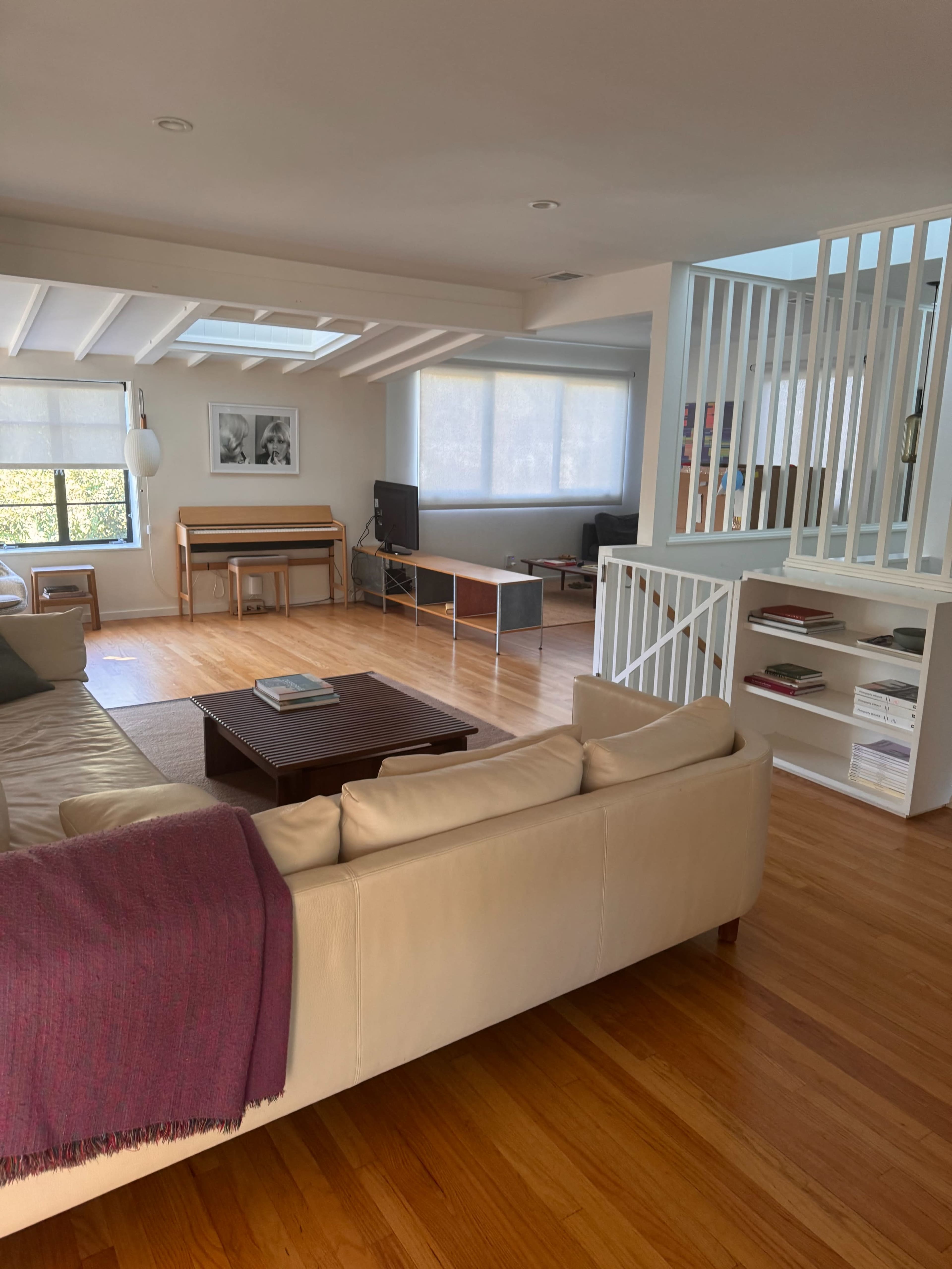 The image shows a modern, open-concept living space featuring a cream-colored sofa, wooden floors, and a dining area with a table in the background.