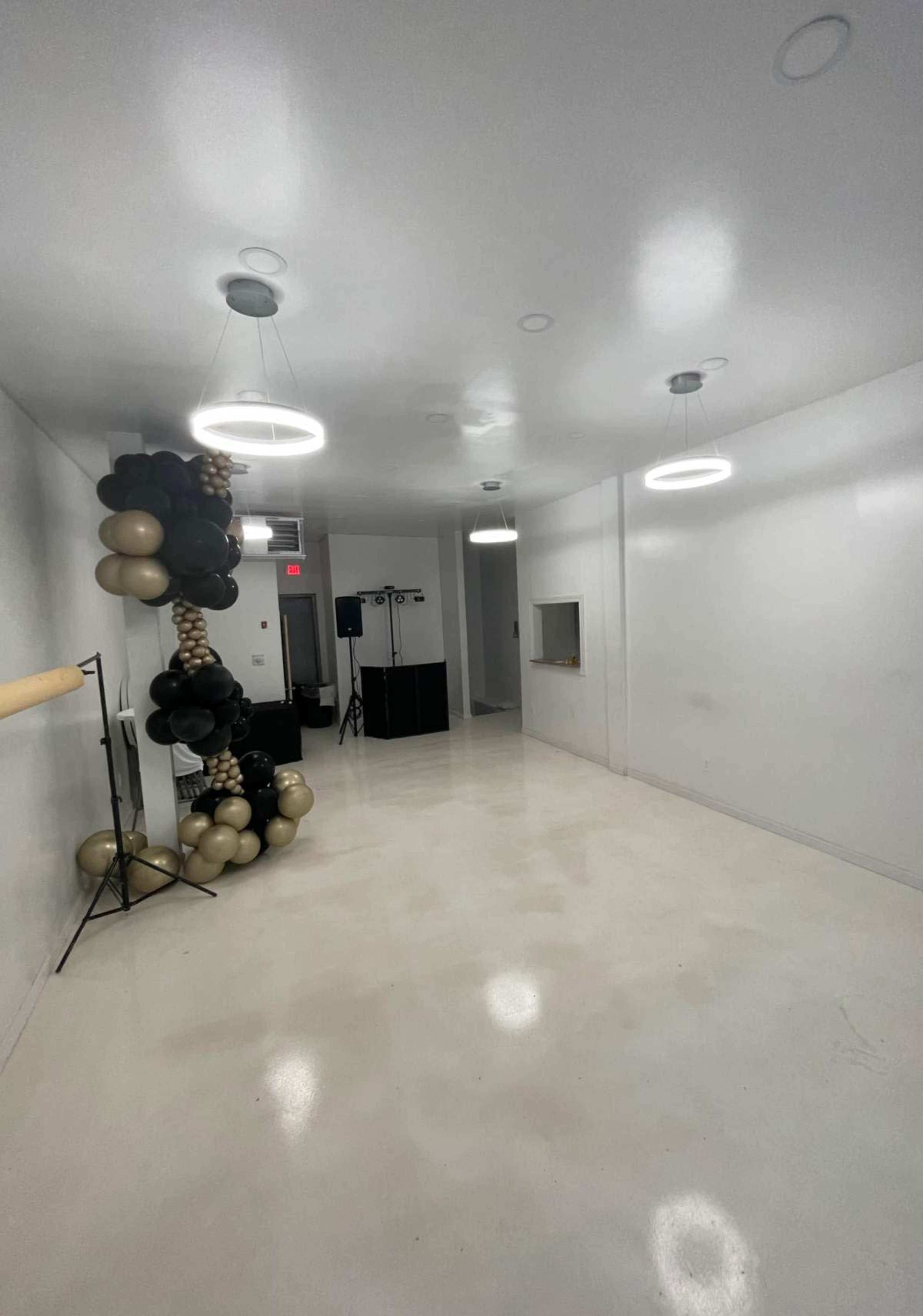 The image shows a spacious, empty room with white walls and a shiny floor, featuring decorative balloons on one wall and modern circular light fixtures.