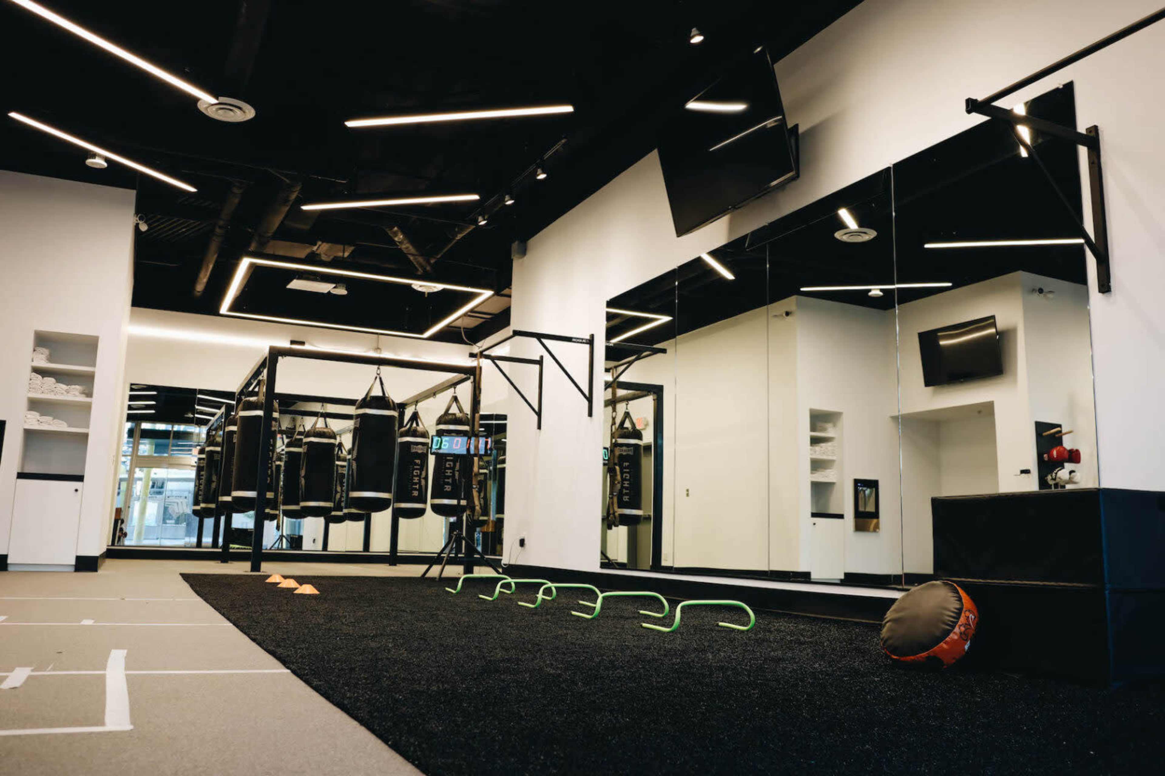 A modern gym interior with boxing bags, fitness equipment, and a mirrored wall.