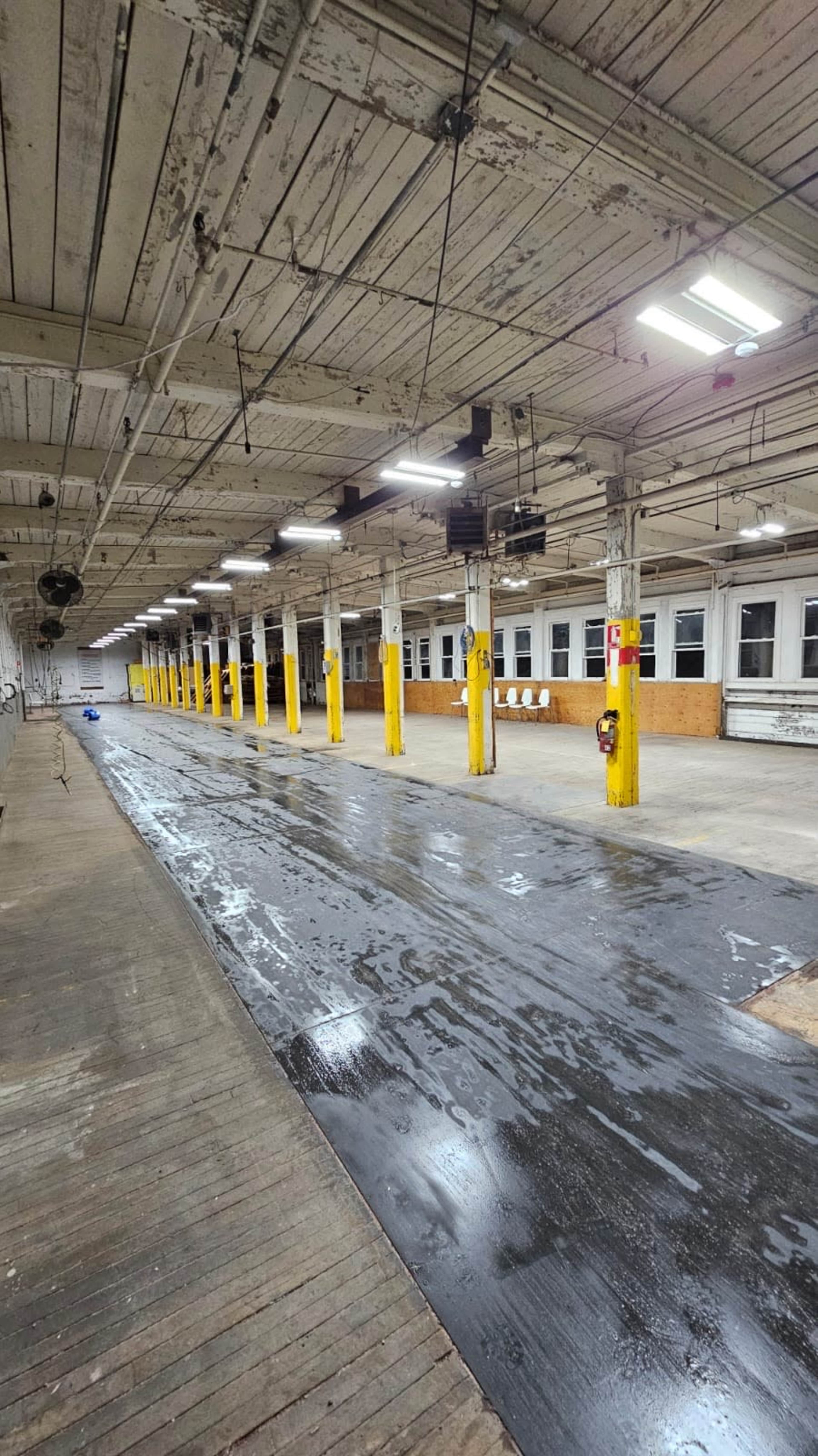 The image shows a large, empty industrial space with rows of yellow support columns and a dark, wet floor.