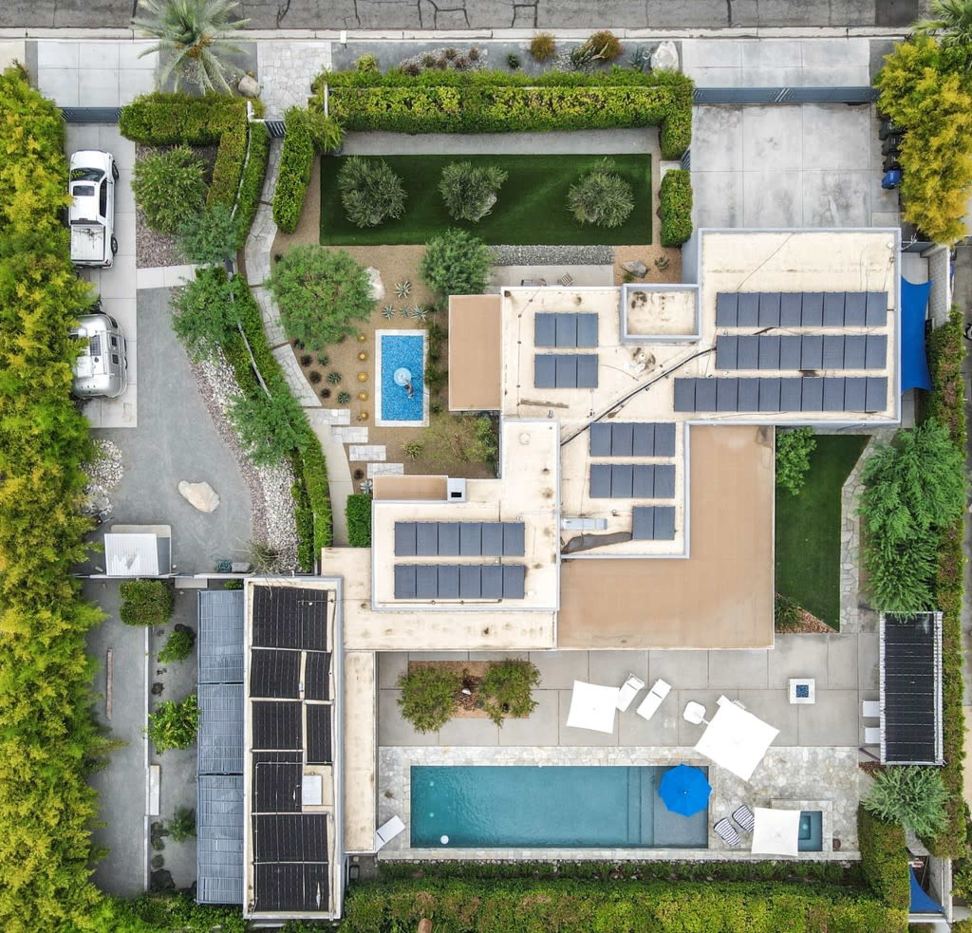 The image shows a modern residential property with a flat roof, solar panels, a swimming pool, and landscaped gardens.