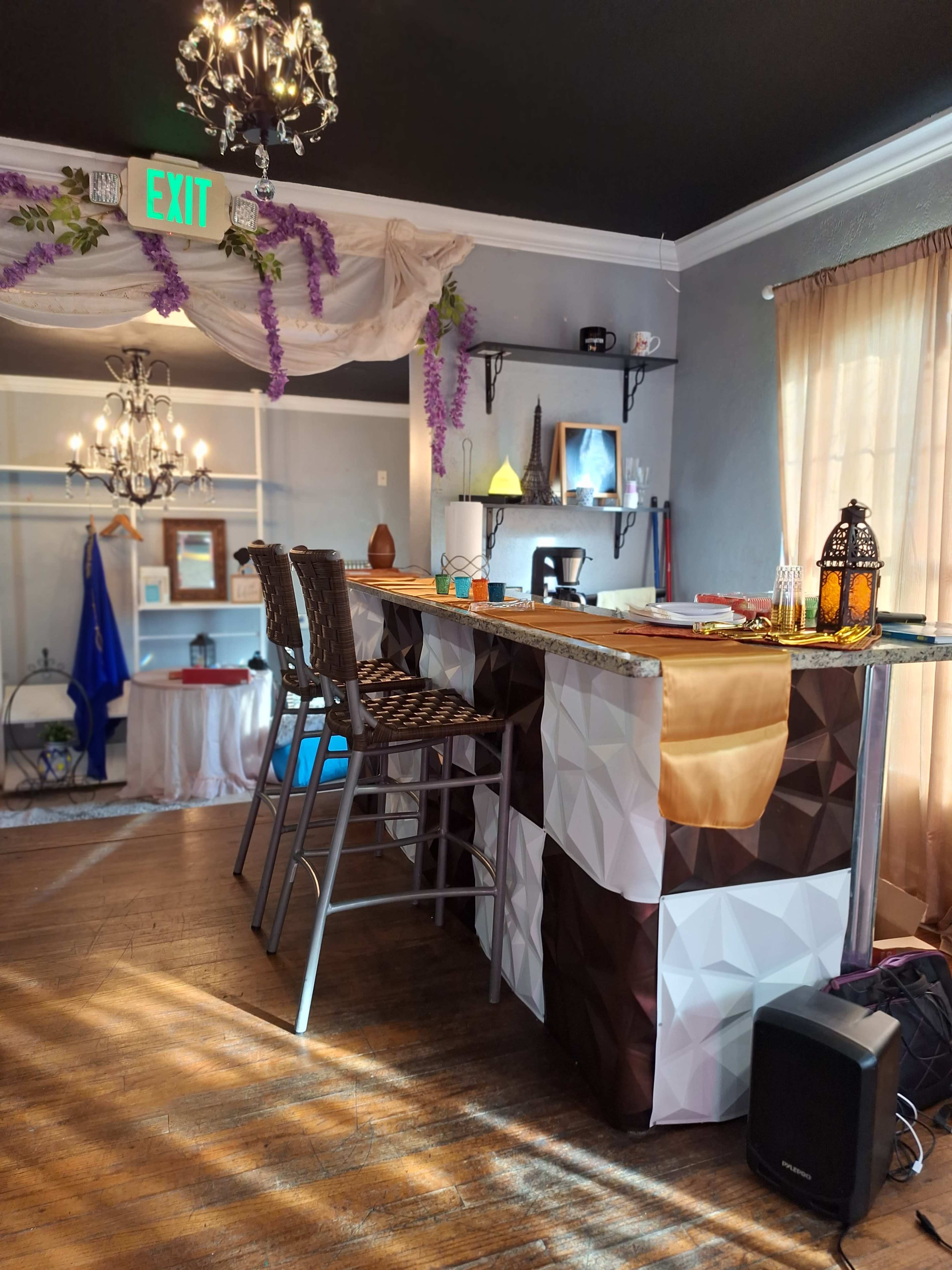 A modern bar area with a geometric-patterned countertop and high stools, decorated with hanging grapevines and a chandelier.