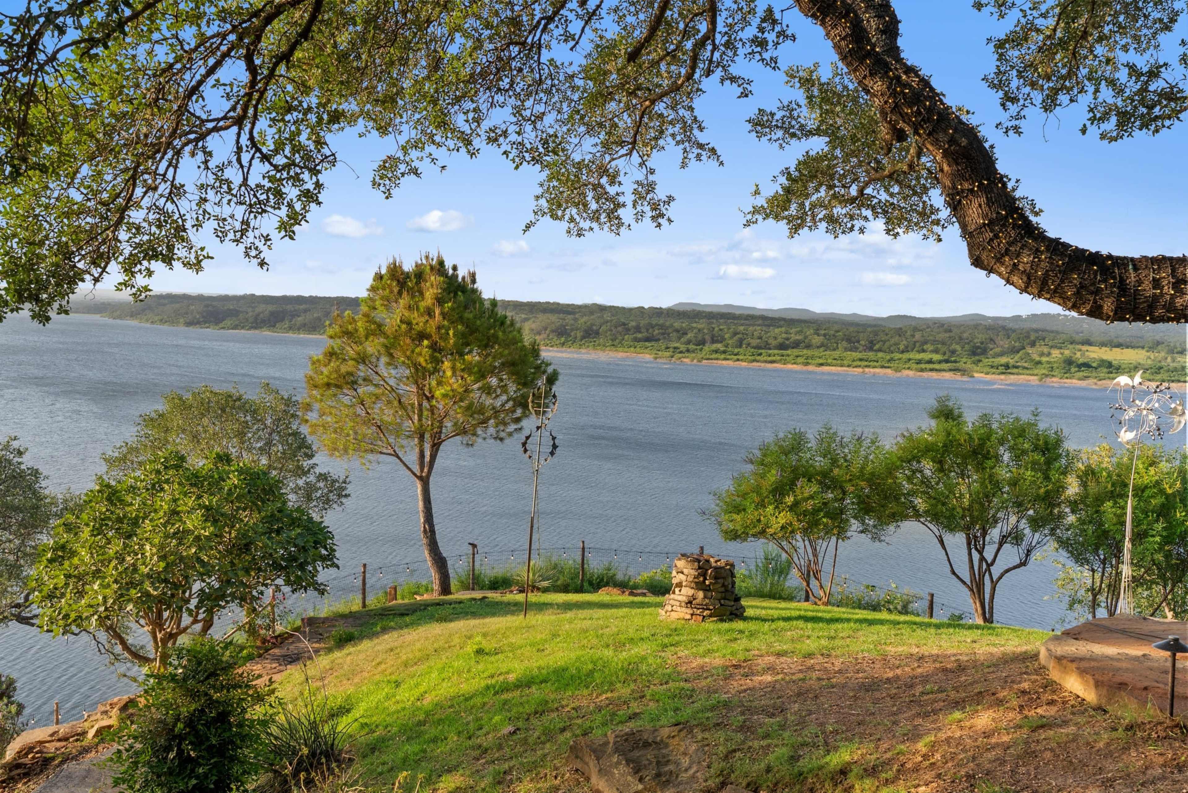 The image shows a grassy area overlooking a calm body of water with trees and hills in the background.