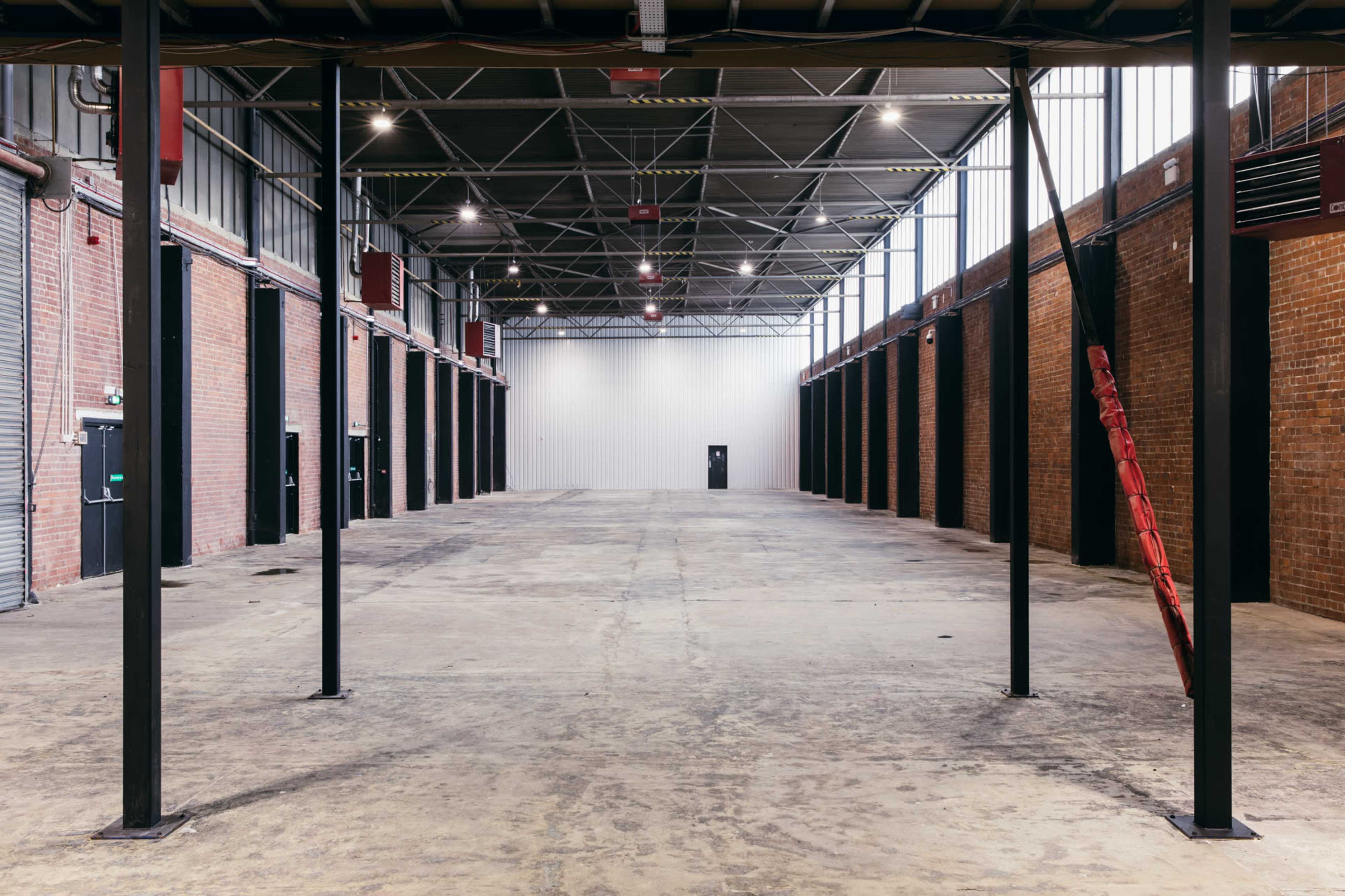 A spacious, empty industrial warehouse with high ceilings, exposed brick walls, and a single door at the far end.