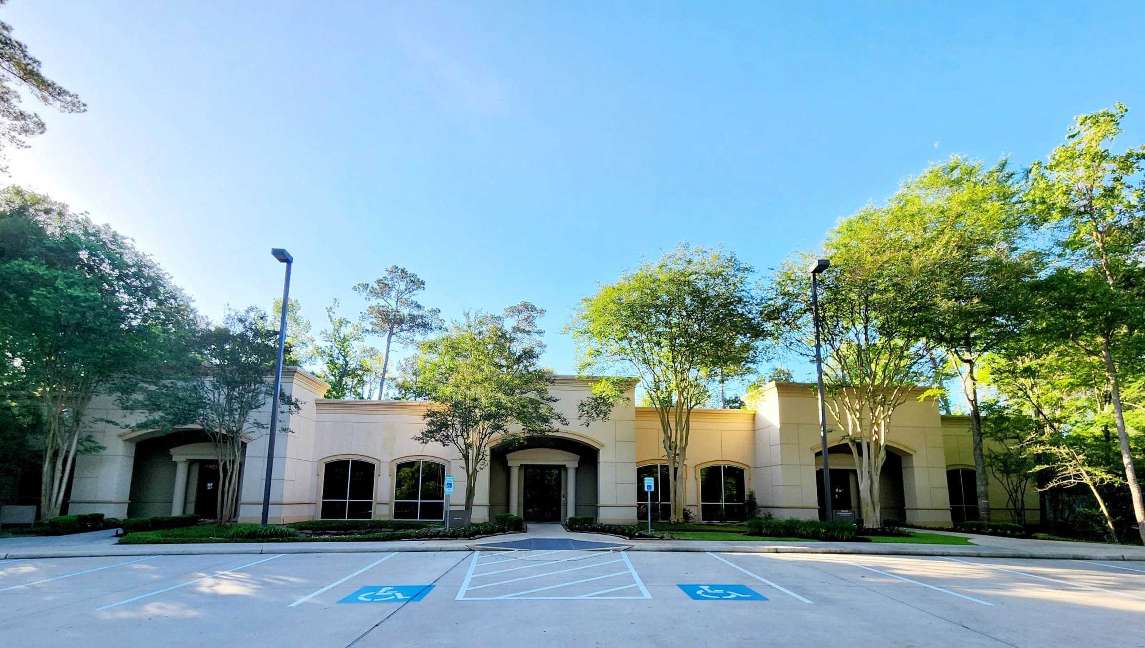 A modern building is surrounded by trees and features several parking spaces, including designated handicapped spots.