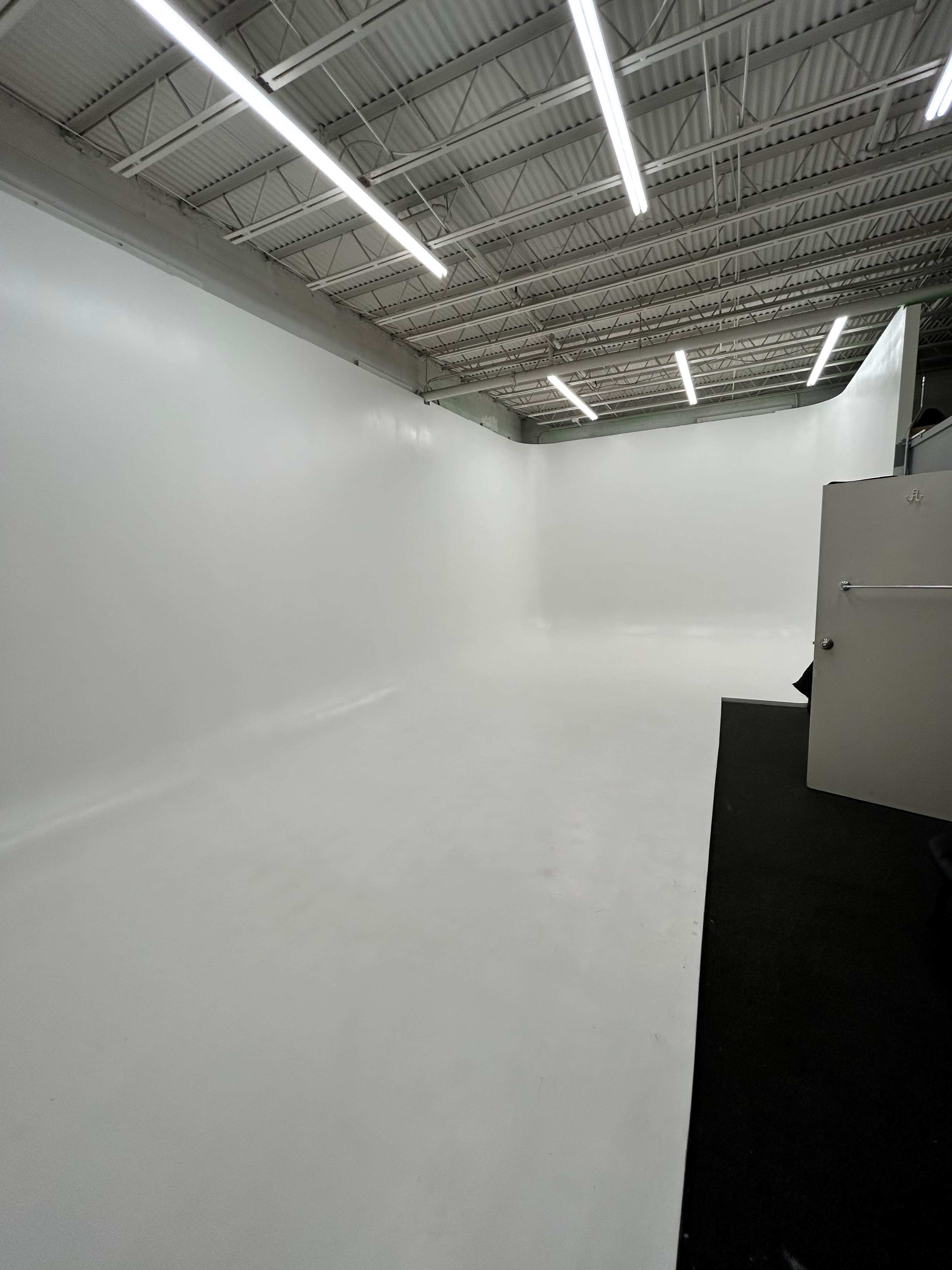 A large, empty studio with white walls and flooring, illuminated by bright overhead lights.