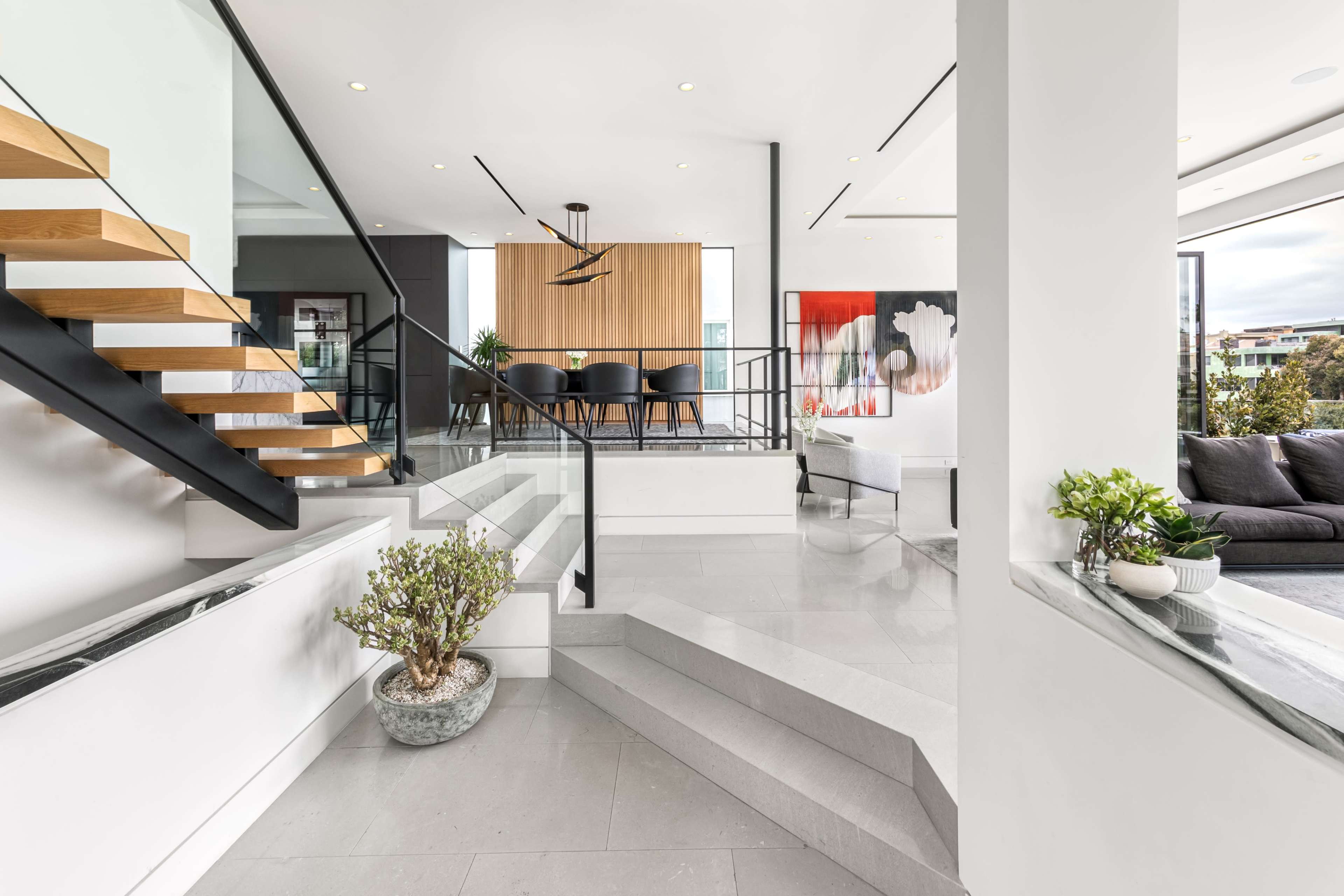 A modern interior featuring a staircase with wooden steps, leading to an open dining area and a living space with large windows.