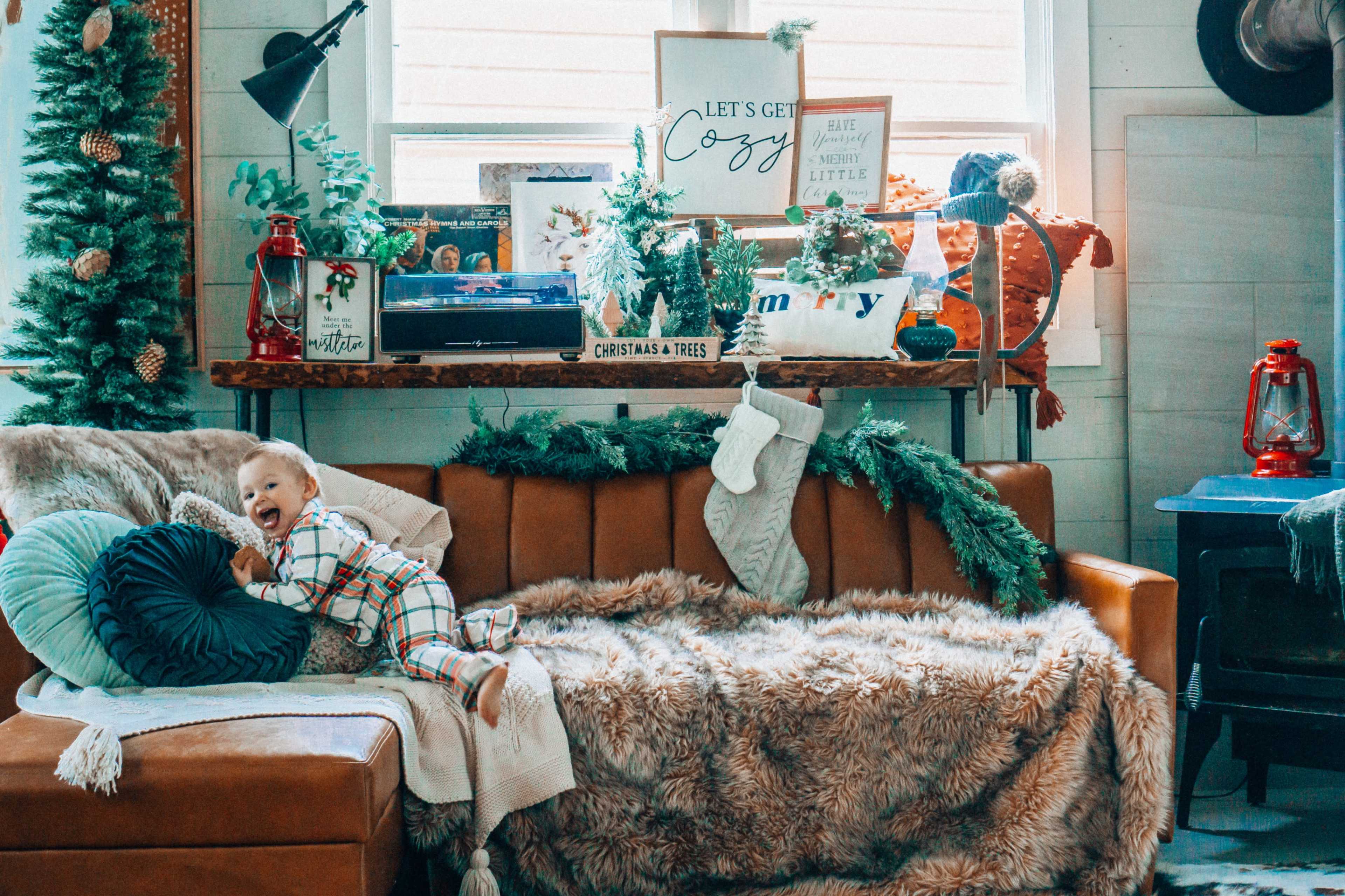 A child in festive pajamas plays on a cozy brown couch adorned with holiday decorations and throws.