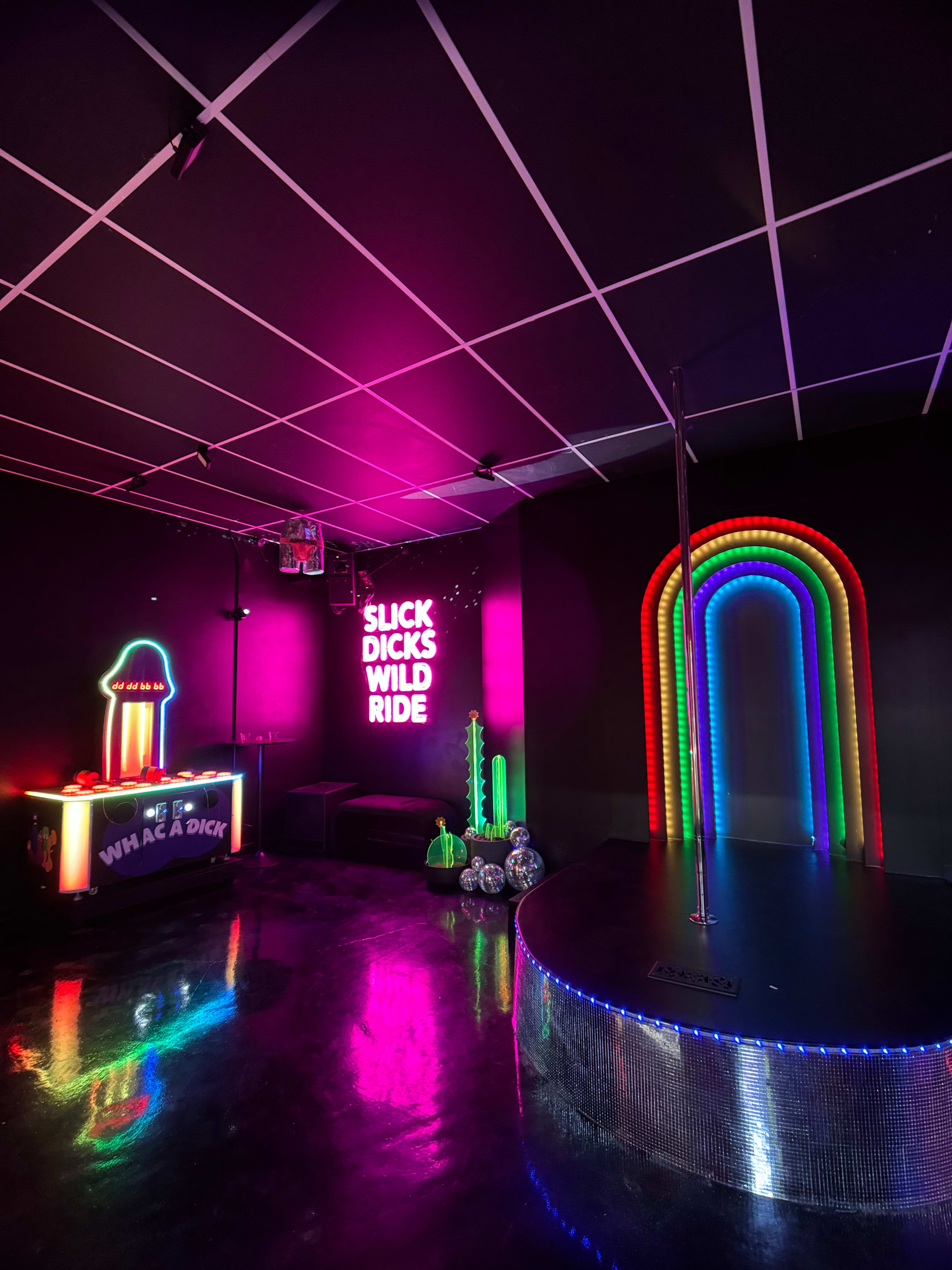 A colorful entertainment venue featuring neon lights, a pole, and playful signage against a dark background.
