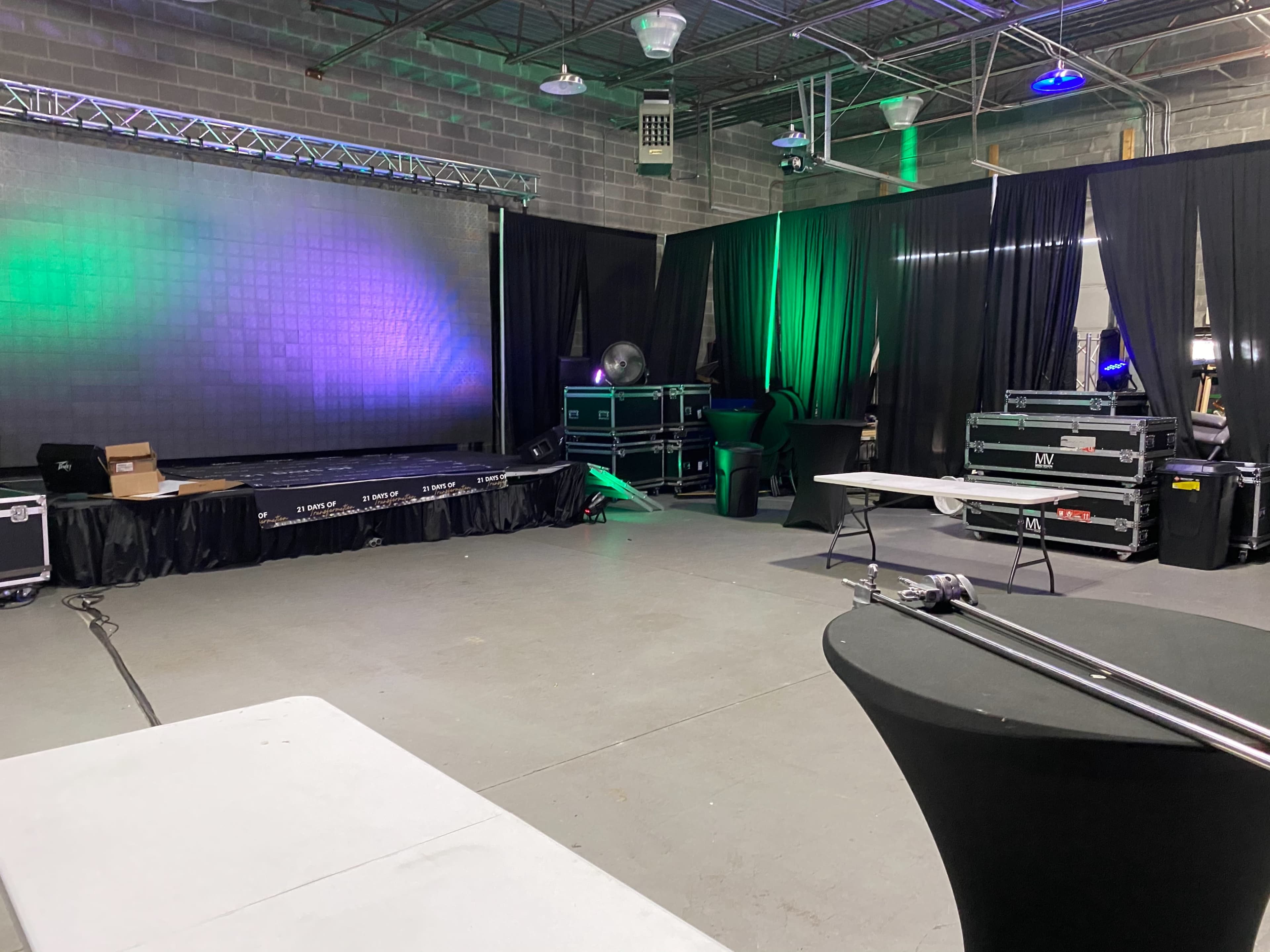 A dimly lit event space with a stage at the back, surrounded by black curtains and various equipment cases.