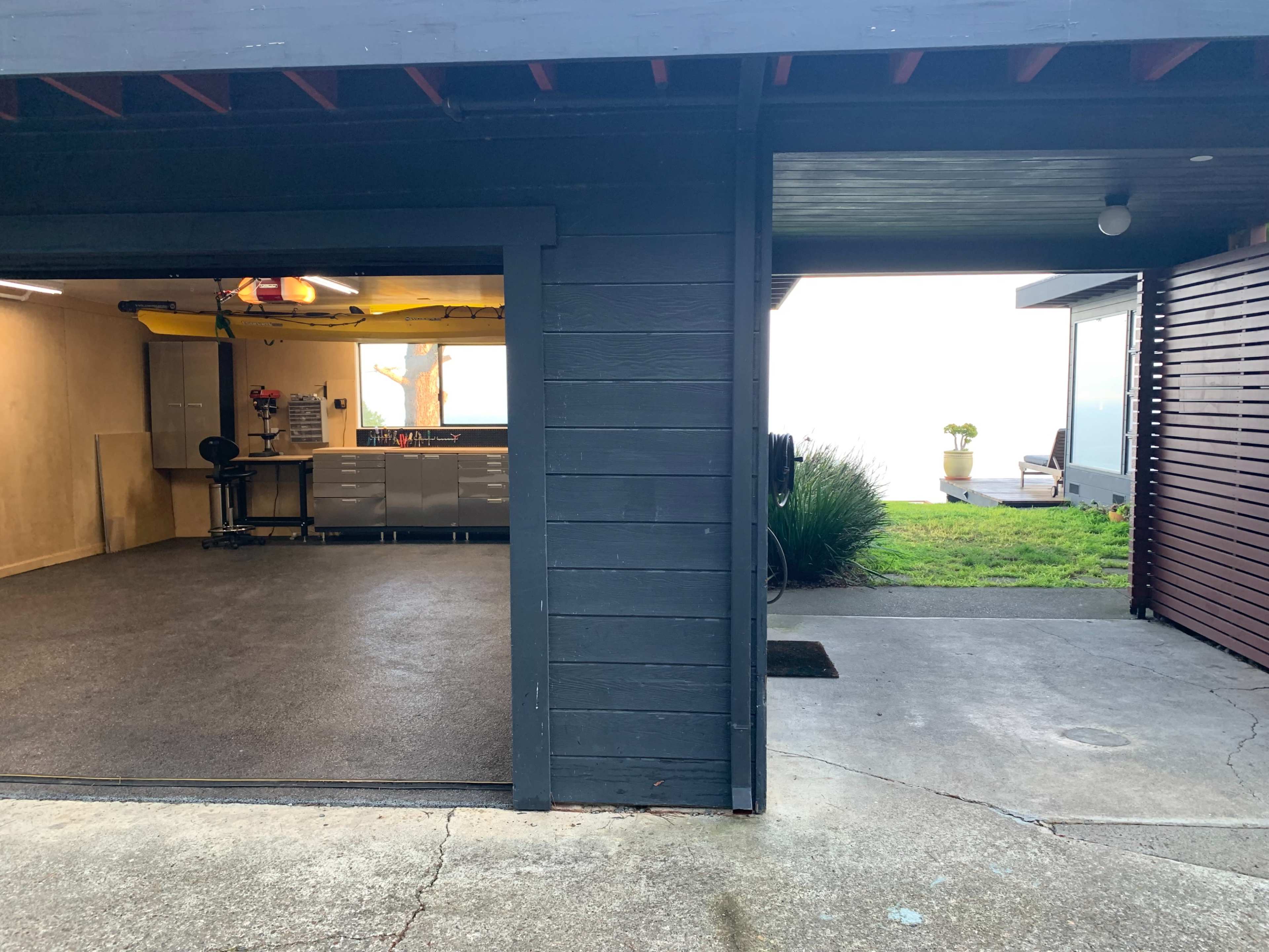 A split view of a garage with a smooth floor and cabinets on one side, and a grassy area leading to a house on the other side.
