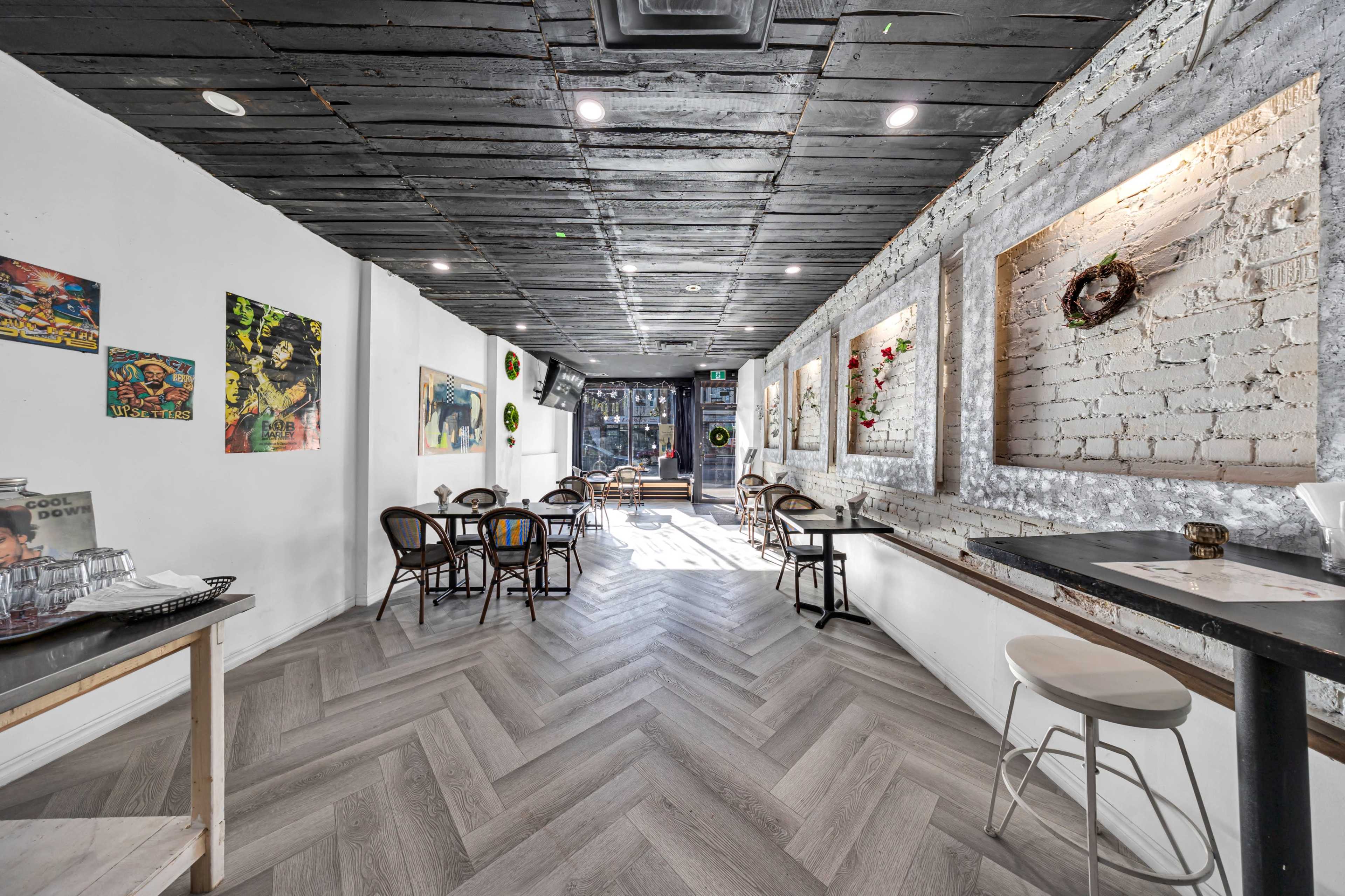 The image shows a narrow, modern café interior with wooden flooring, artwork on the walls, and a mix of seating arrangements.