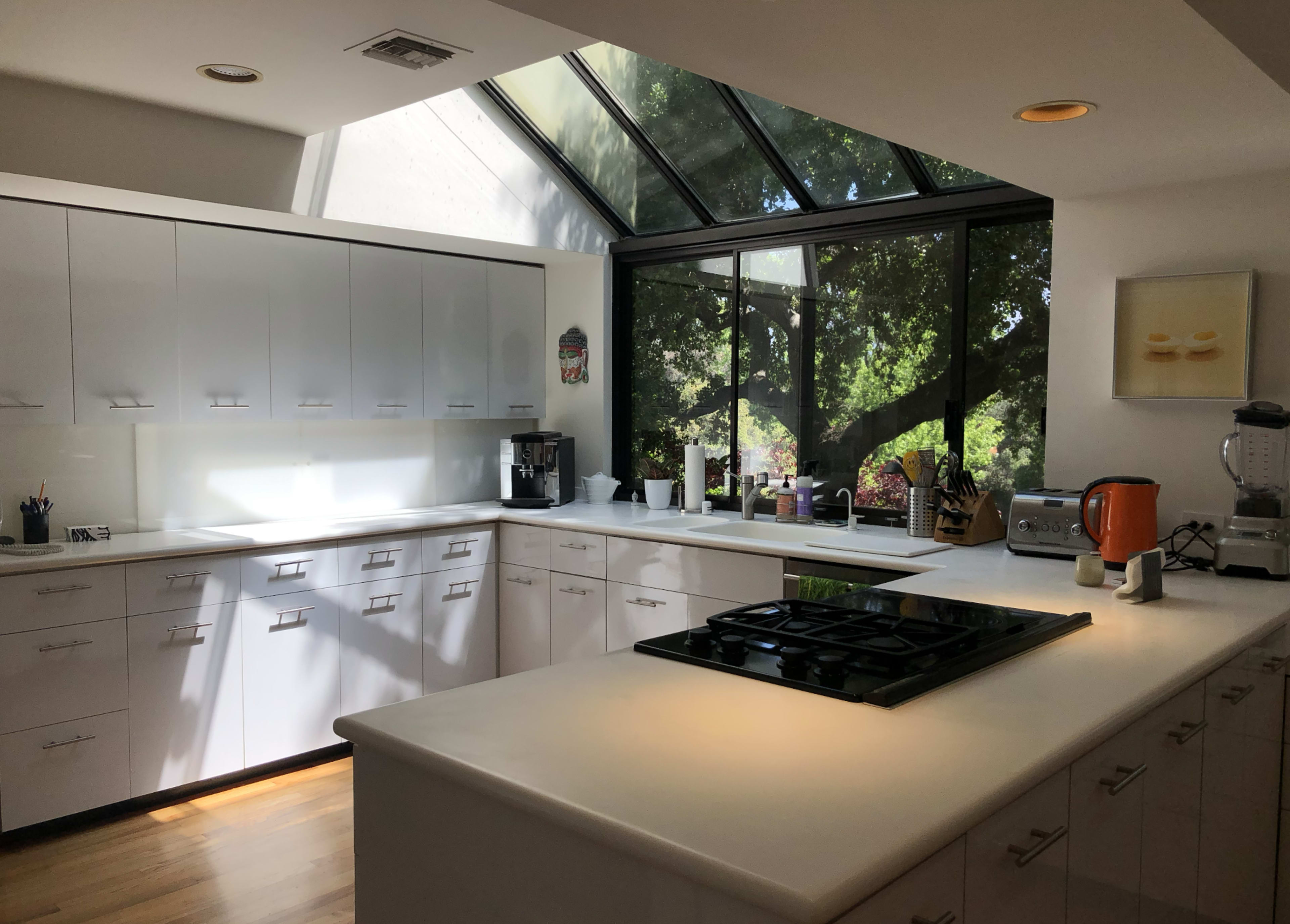 The image shows a modern kitchen with white cabinets, a gas stove, and large windows allowing natural light to illuminate the space.