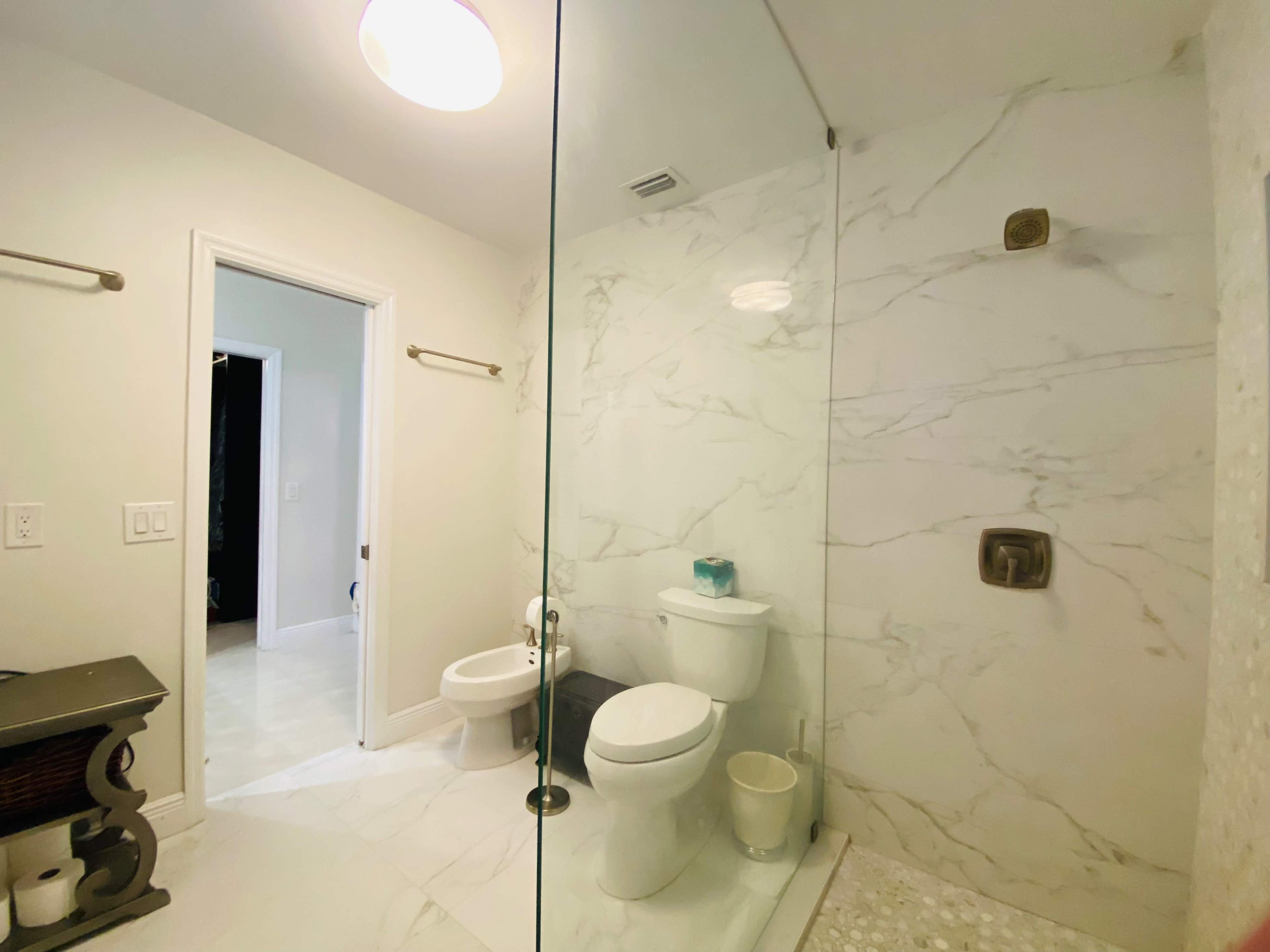 The image shows a modern bathroom with a glass shower enclosure, a toilet, and marble-patterned walls.