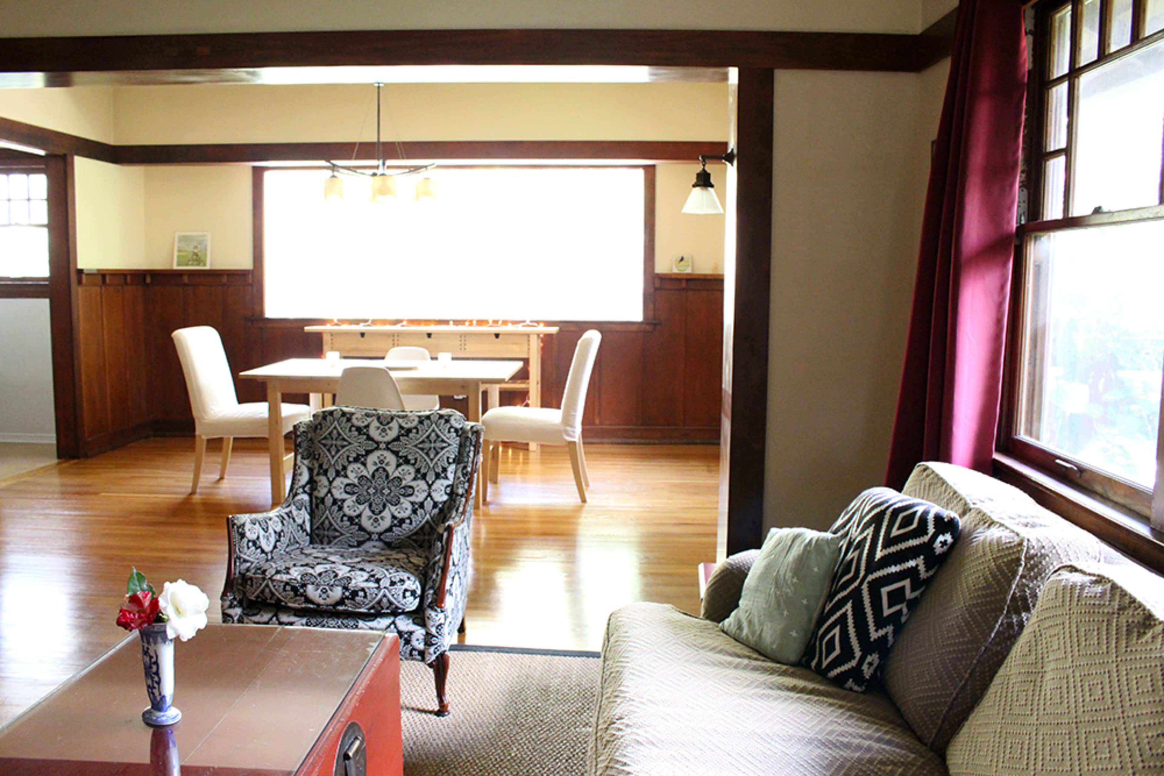 The image shows a living room with a patterned armchair, sofa, and a visible dining area featuring a table and white chairs in the background.