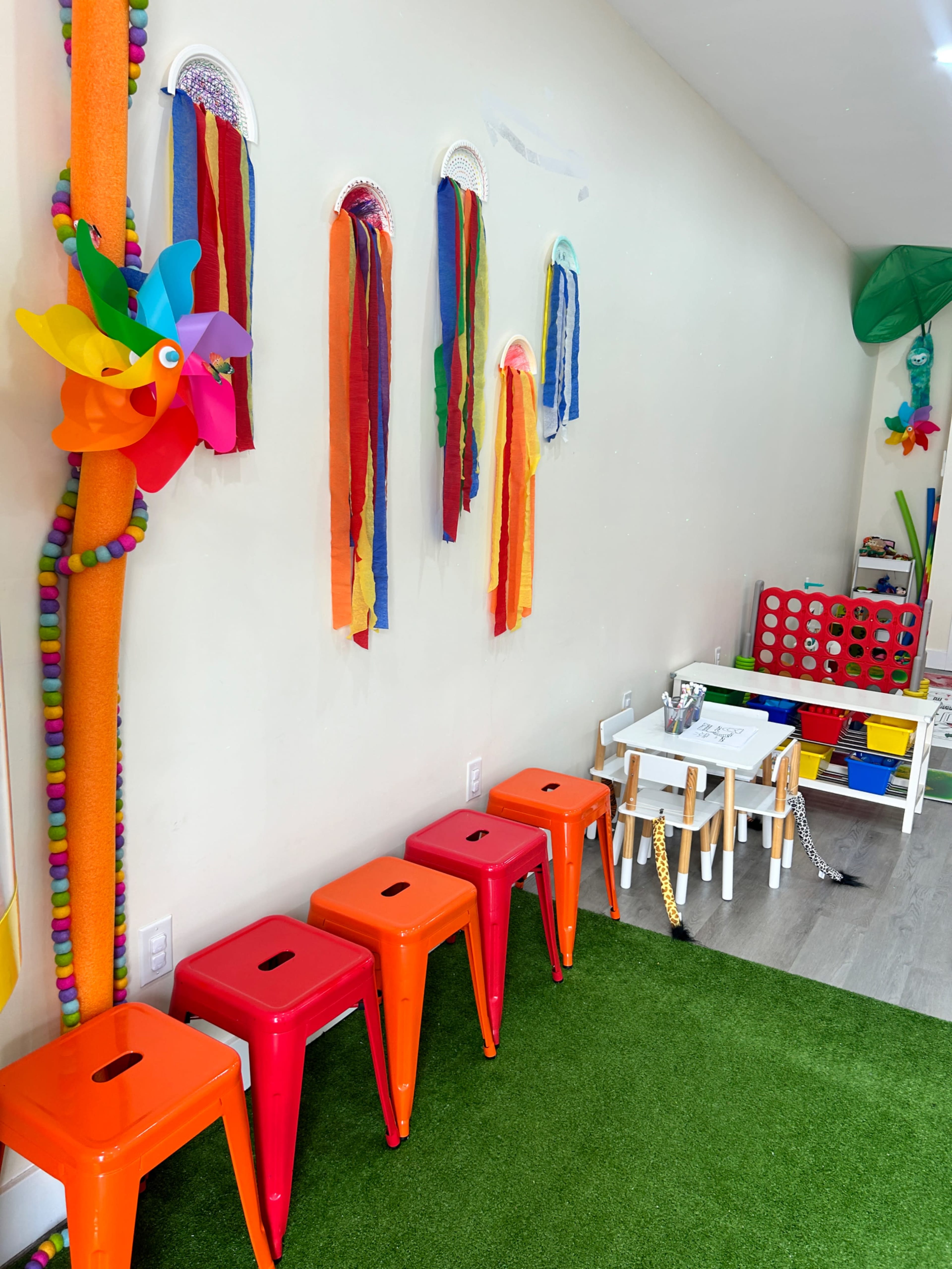 A colorful playroom setup with bright stools, decorative ribbons, and a children's table with games.