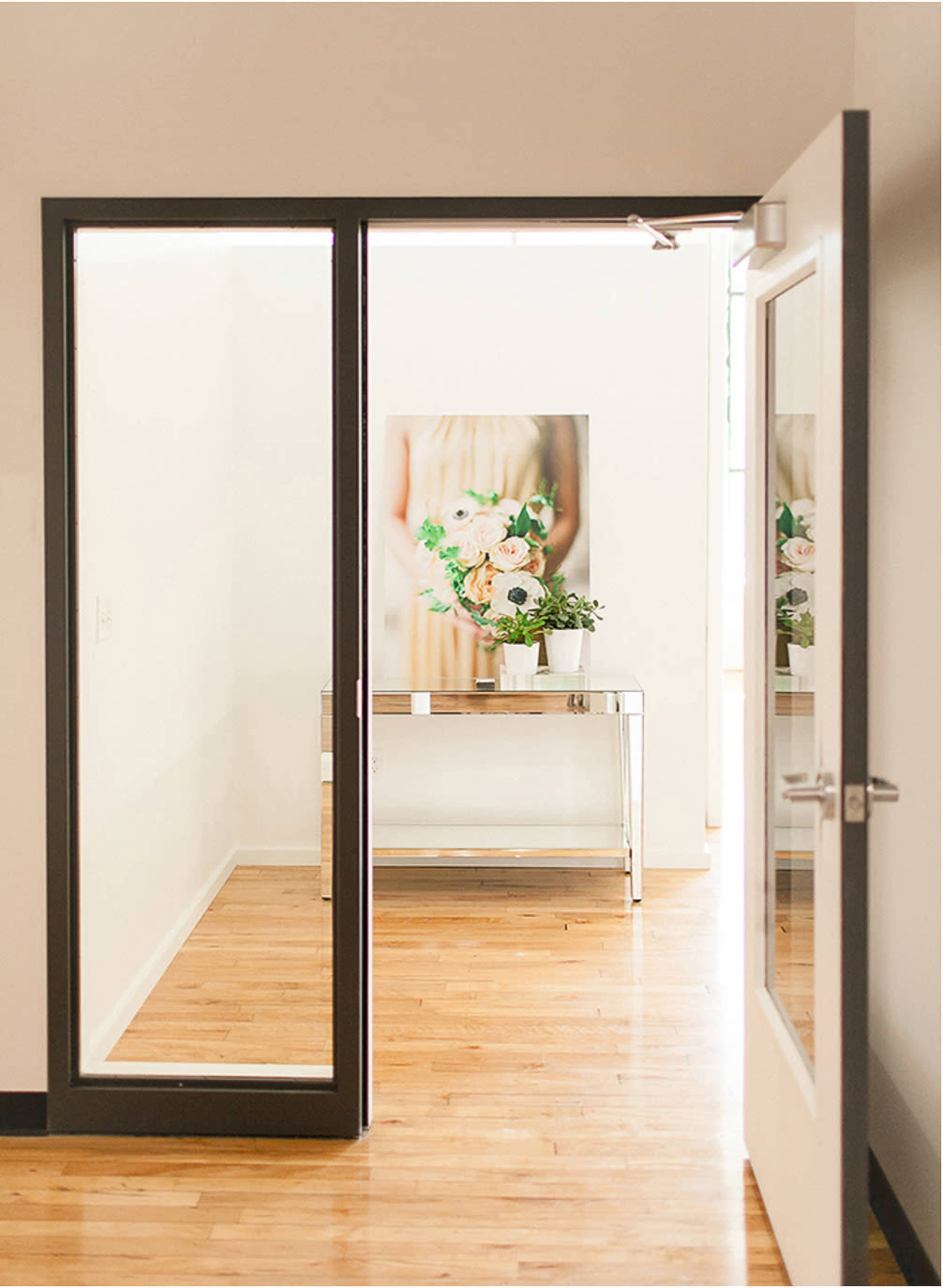 A partially open door reveals a bright room with a decorative table and a floral artwork on the wall.