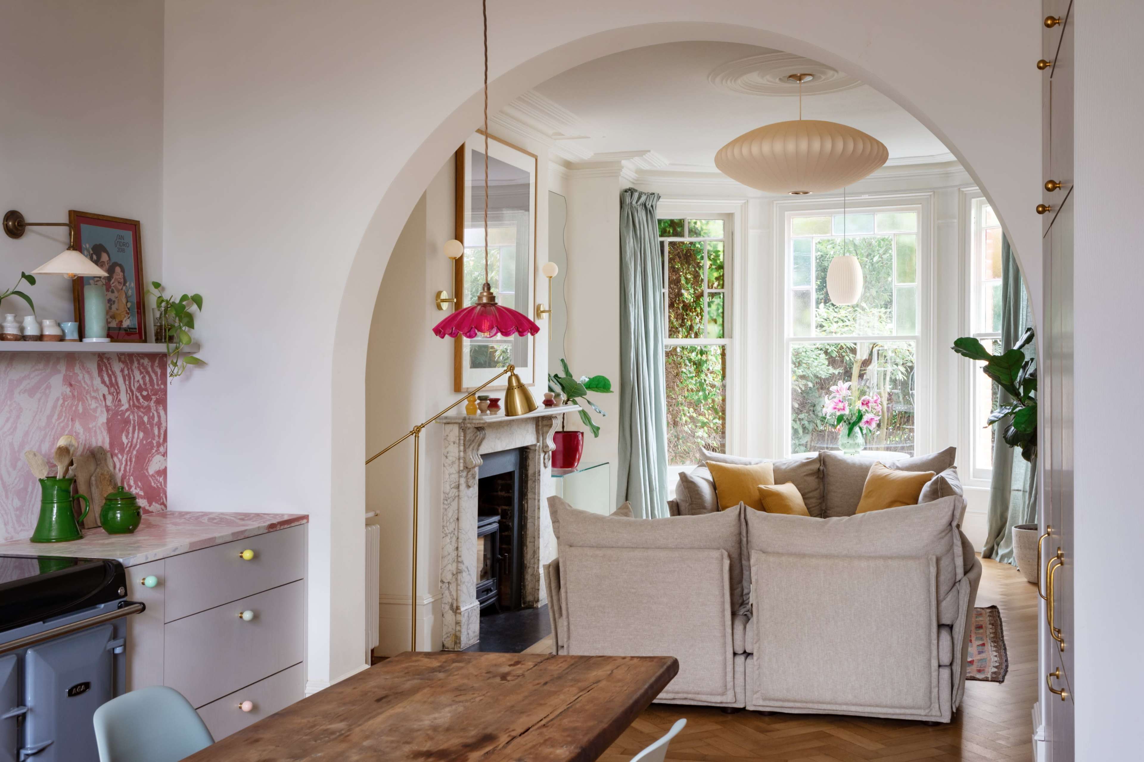 A cozy living space features a large bay window, a soft sofa with yellow cushions, and a dining area with a wooden table and colorful kitchen accents.