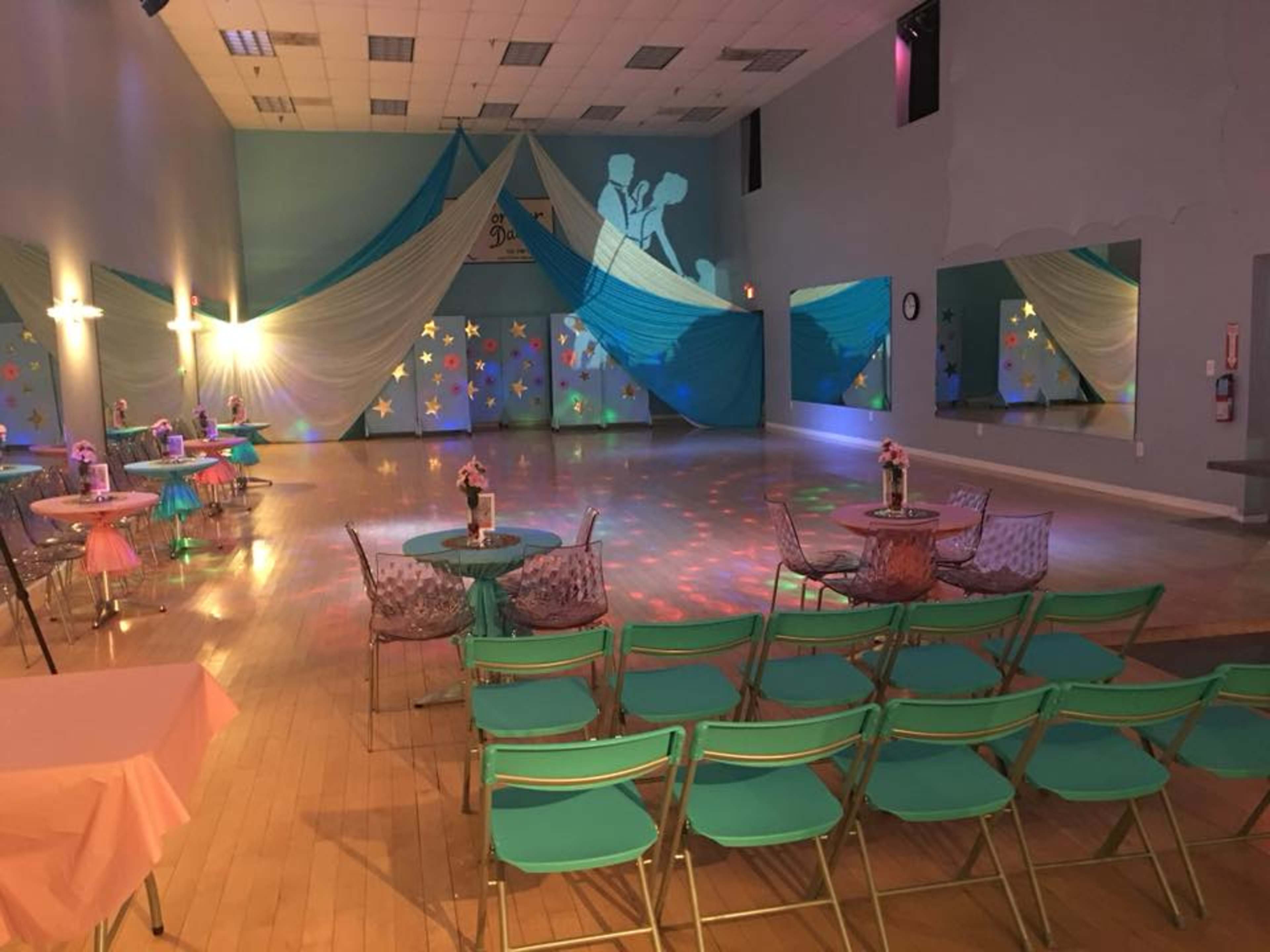 A dance hall setup with decorated tables, chairs, and colorful drapery on the walls.