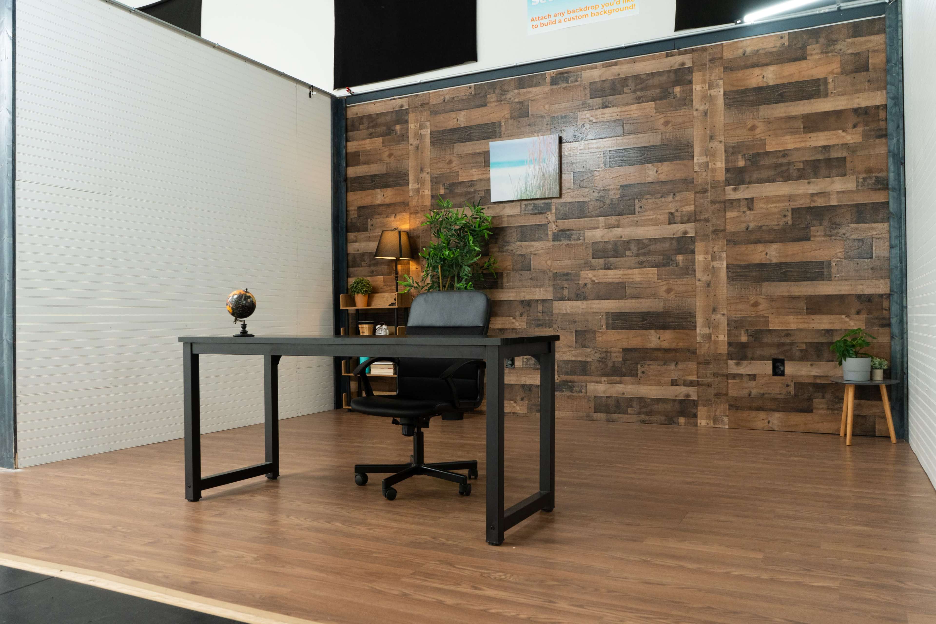 A minimalistic office space with a wooden accent wall, a black desk and chair, a globe, and a small plant.