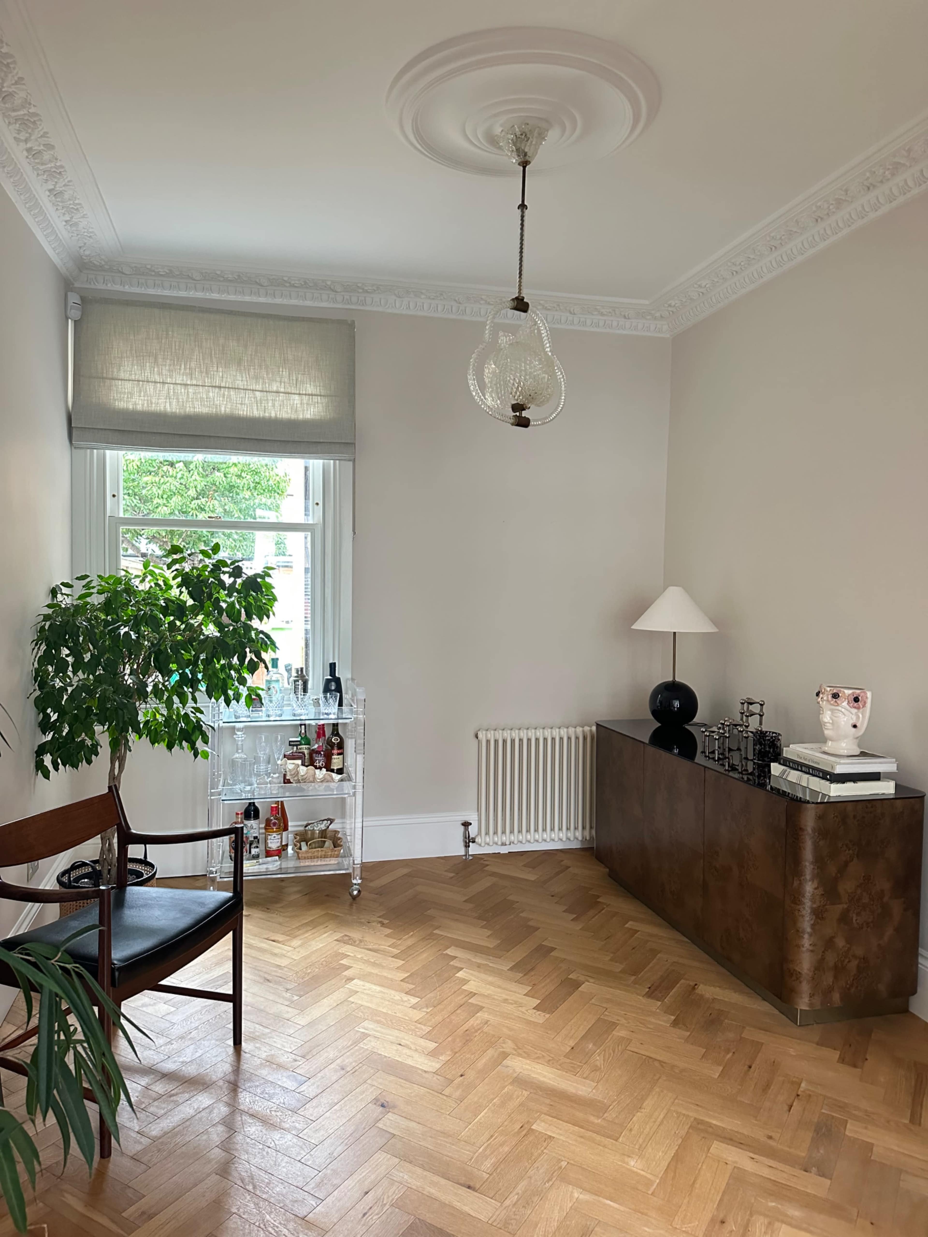 The room features a wooden floor, a bar cart with bottles, a lamp, a chair, and a decorative plant.
