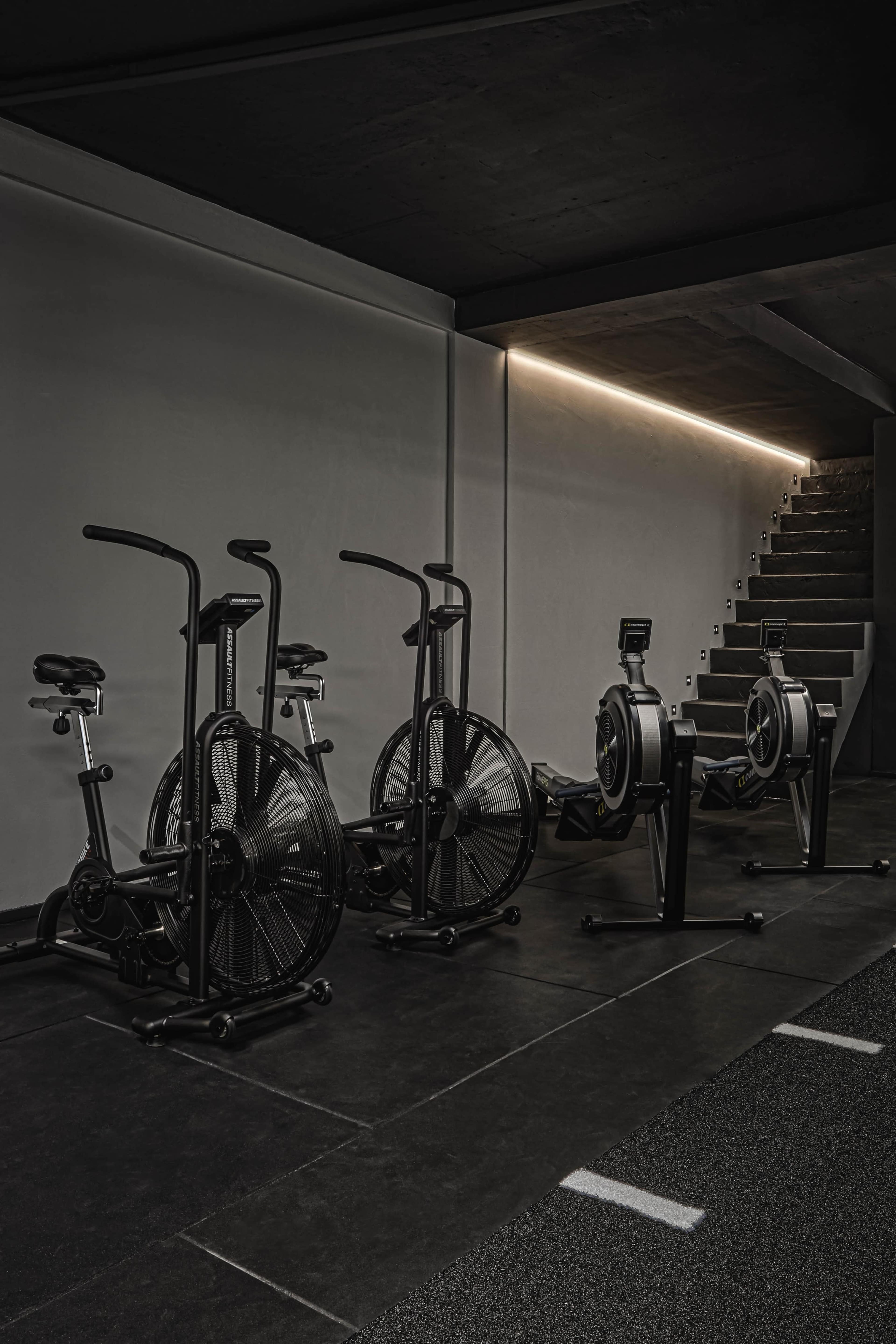 A fitness studio with four exercise machines arranged against a wall and a staircase in the background.
